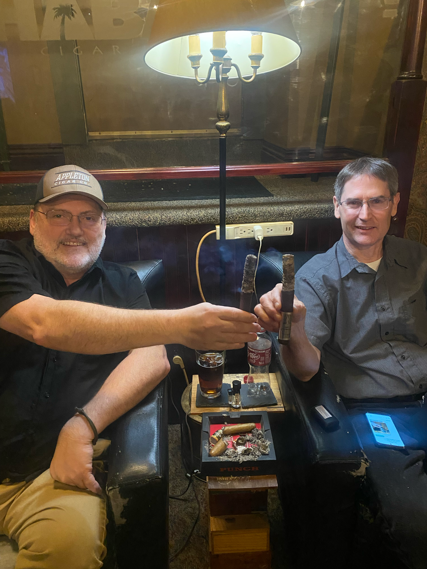 Two men are sitting in chairs toasting with cigars.