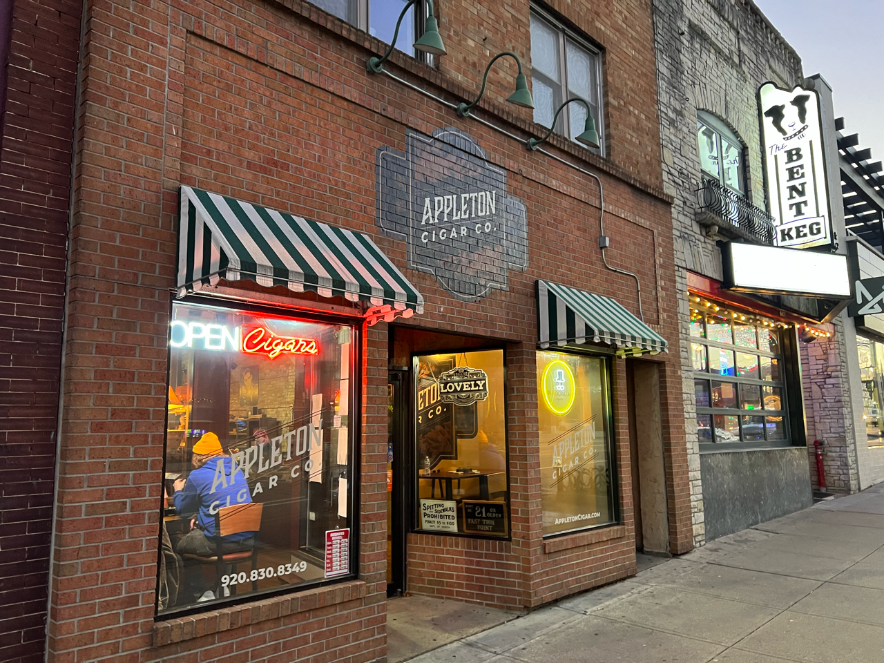 A brick building with a green and white awning and a neon sign.