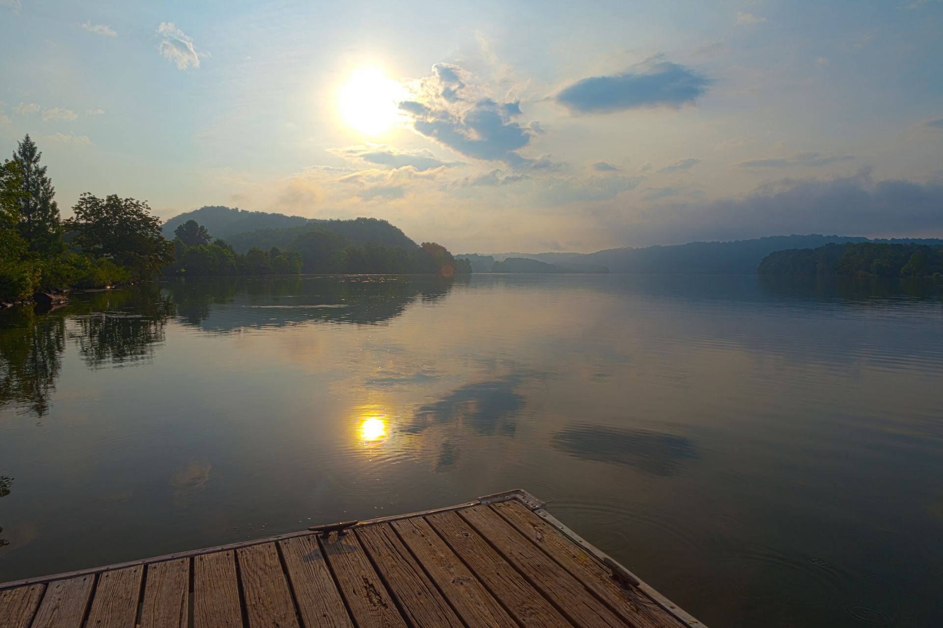 Sunrise over a calm lake with mist, reflecting on the water beside a wooden dock