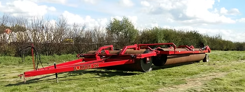 Red agricultural mower or hay implement on a grassy field under a cloudy sky