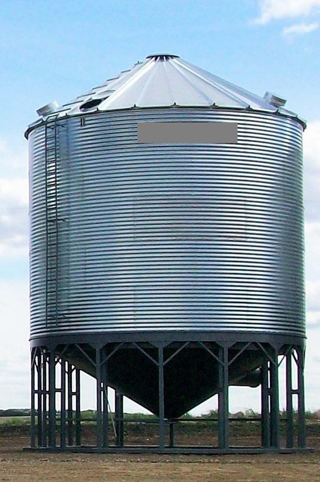 Large silver grain silo on metal stilts against a blue sky