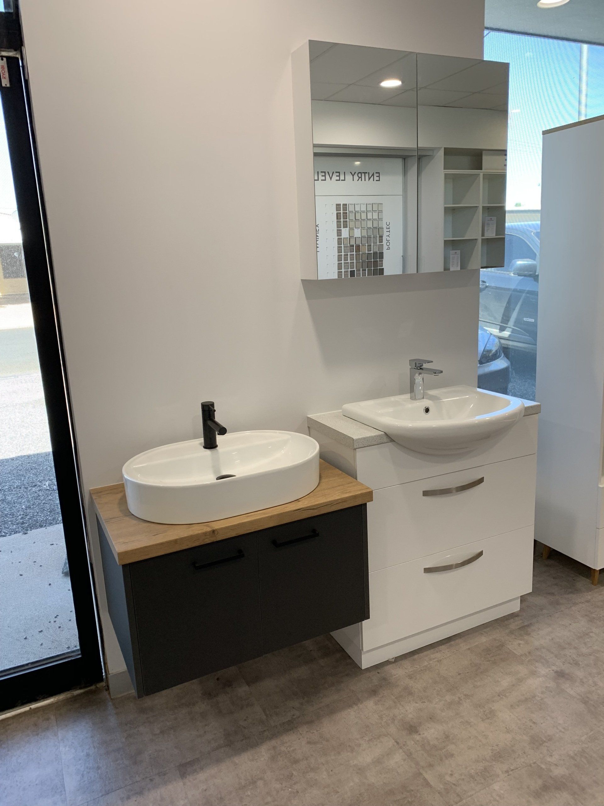 Bathroom vanities, one dark grey with wooden top, one white, with mirrored medicine cabinet.