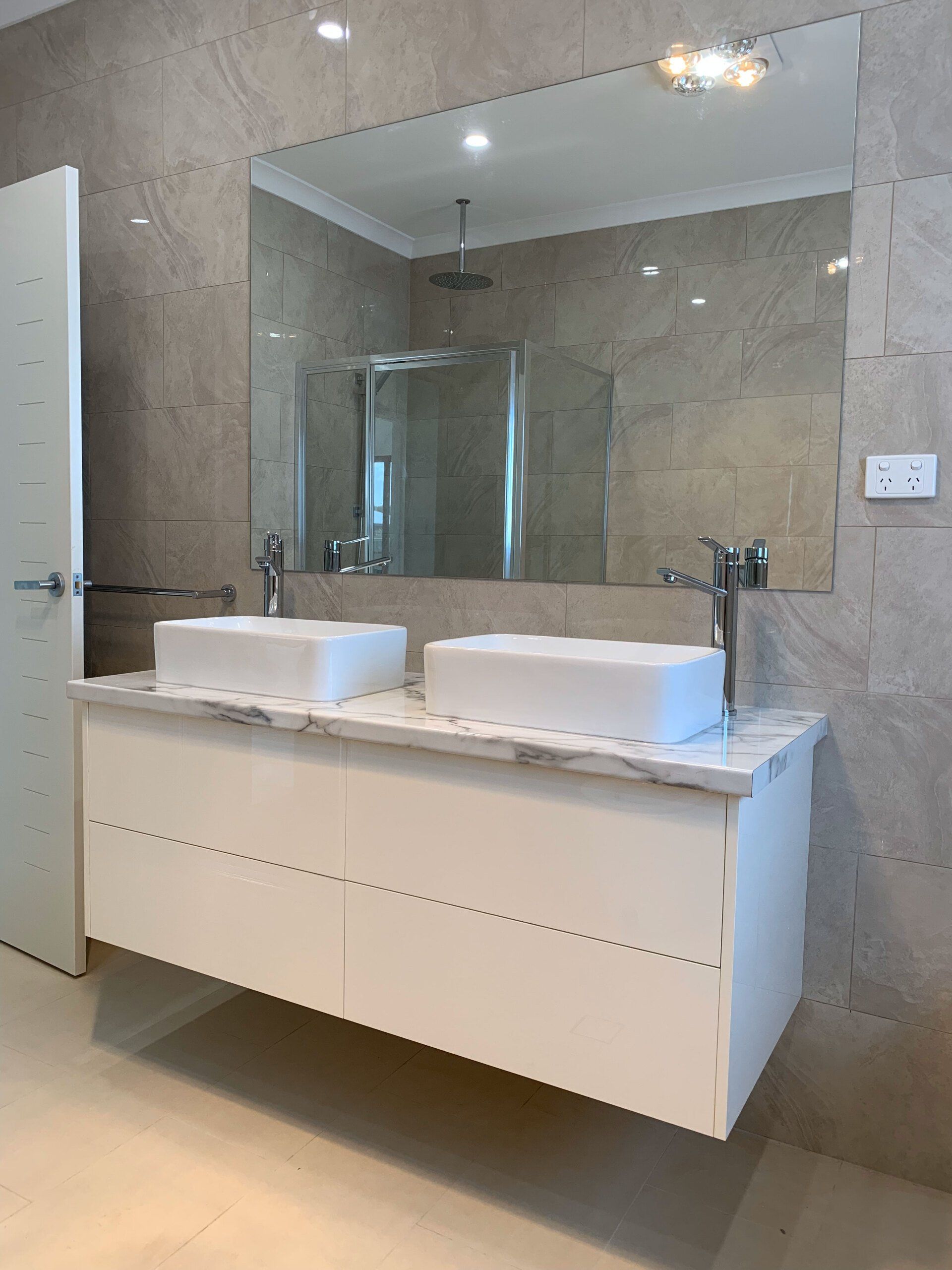 Modern bathroom with floating white vanity, two sinks, large mirror, and glass shower.