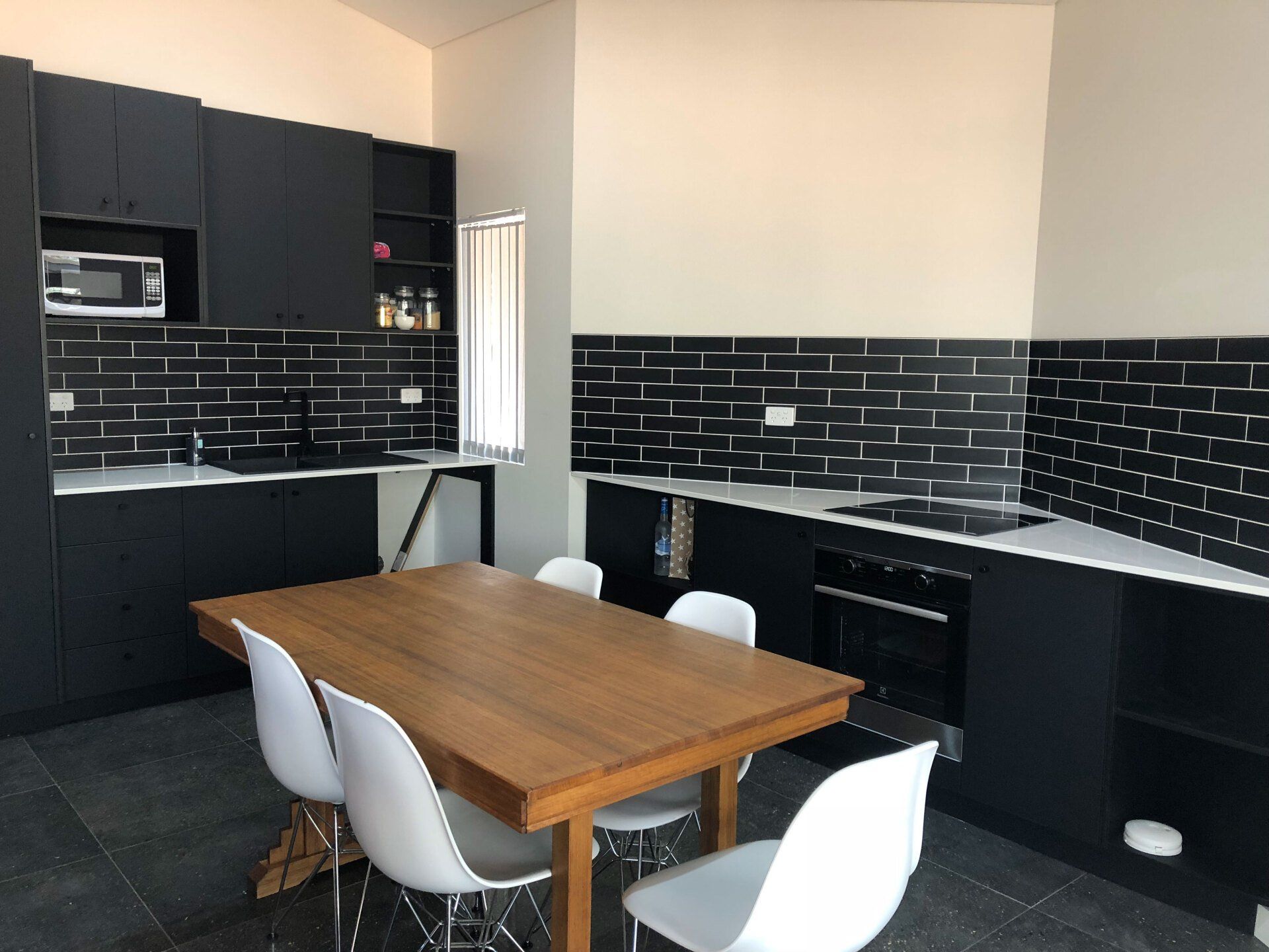Kitchen with black cabinets, white countertops, black tiled backsplash, and wooden dining table with white chairs.