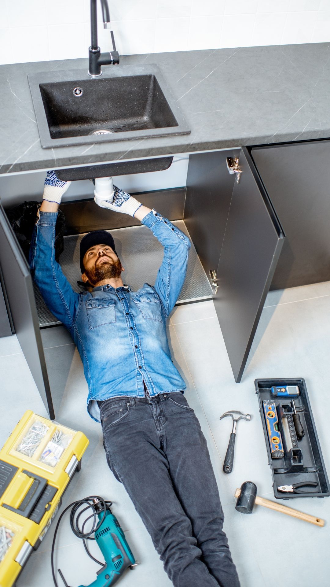 A man is laying on the floor under a kitchen sink.