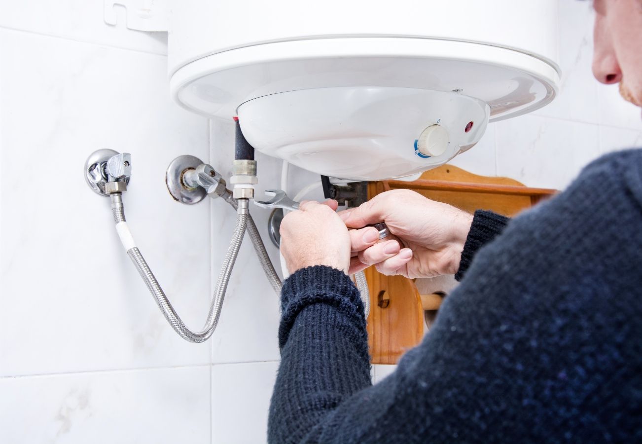 A man is fixing a water heater in a bathroom.