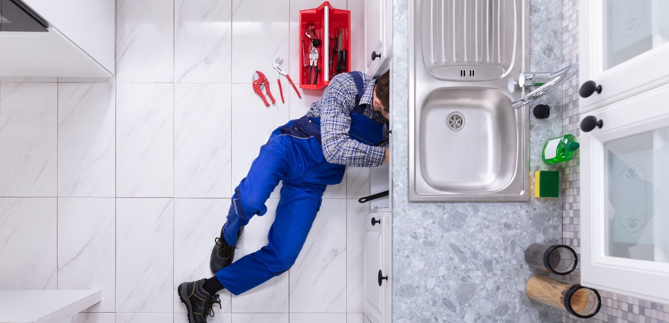 A plumber is fixing a sink pipe with a wrench.