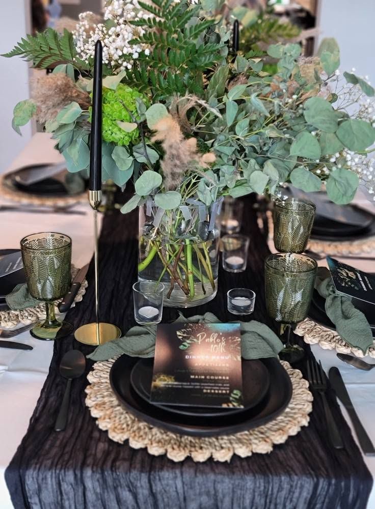 Elegant black-and-gold table setting with greenery centerpiece and candle holders