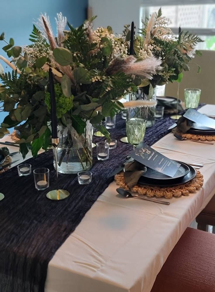 Dining table set with dark runner, cream tablecloth, glassware, candles, and floral centerpieces
