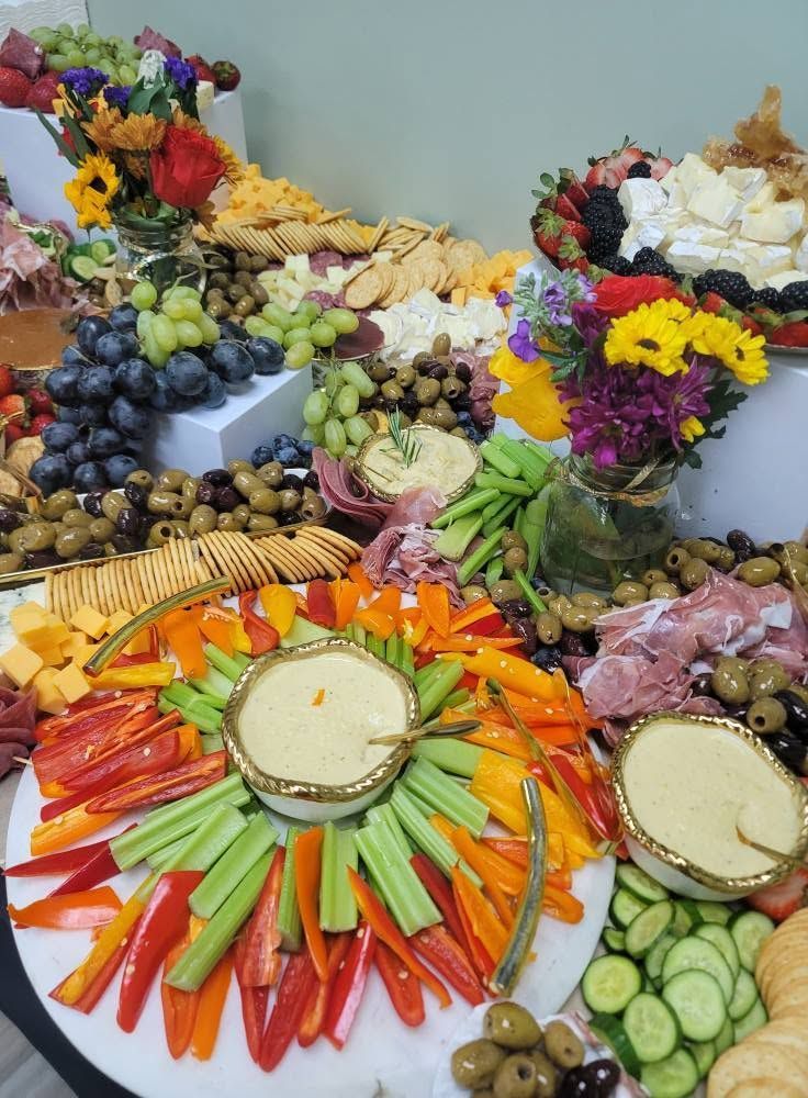 Colorful fruit and vegetable platter arranged around flowers on a table, with cucumbers, peppers, and dip bowls