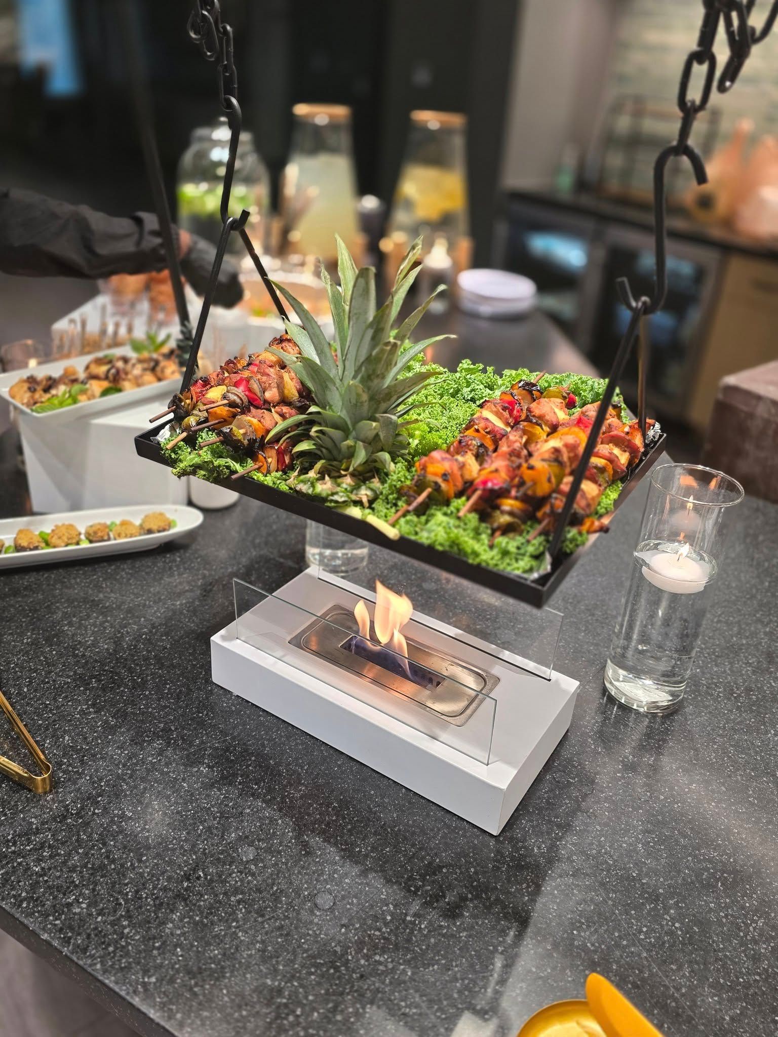 Suspended buffet tray with tropical fruit centerpiece over a dark speckled table, lit by candles