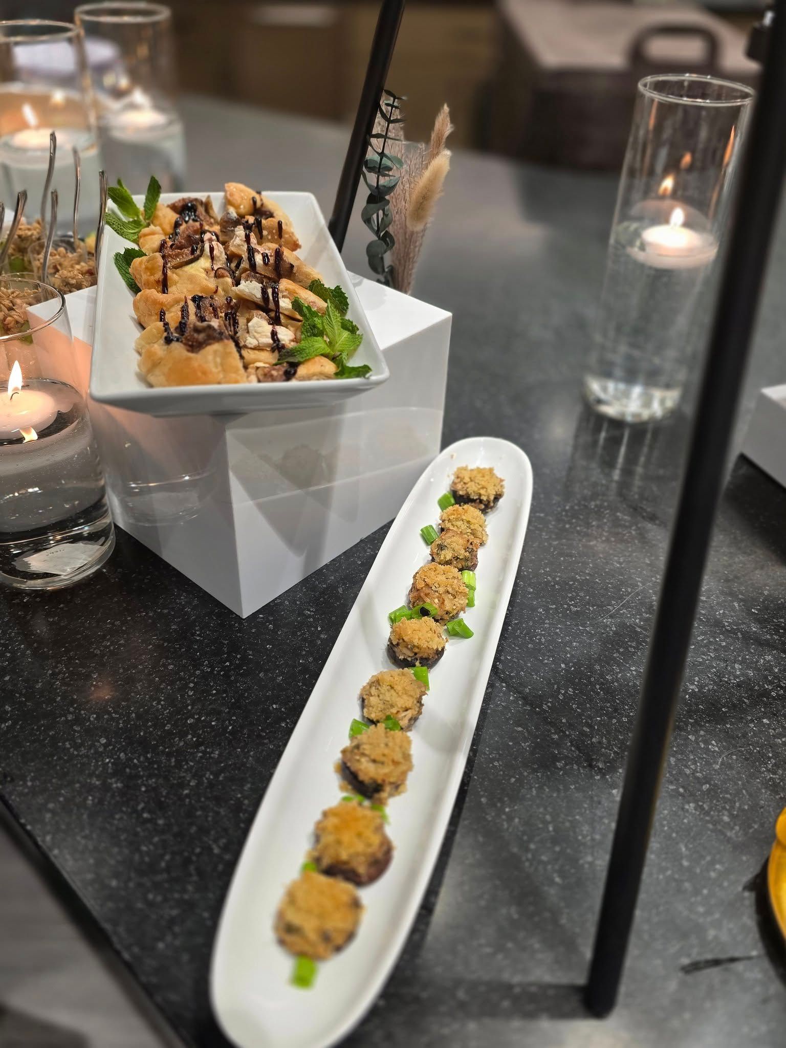 Elegant appetizer spread on a table: sushi rolls on white dishes and a square bowl of mixed bites with drizzle.