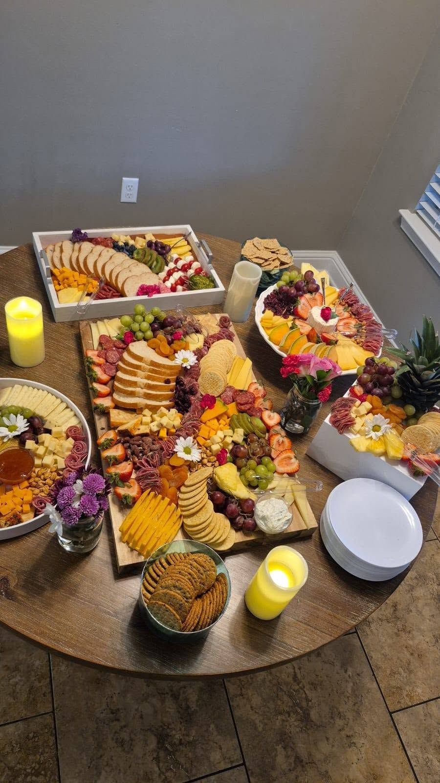 Round table with assorted charcuterie, fruit, cheese, and candles in a dining room.