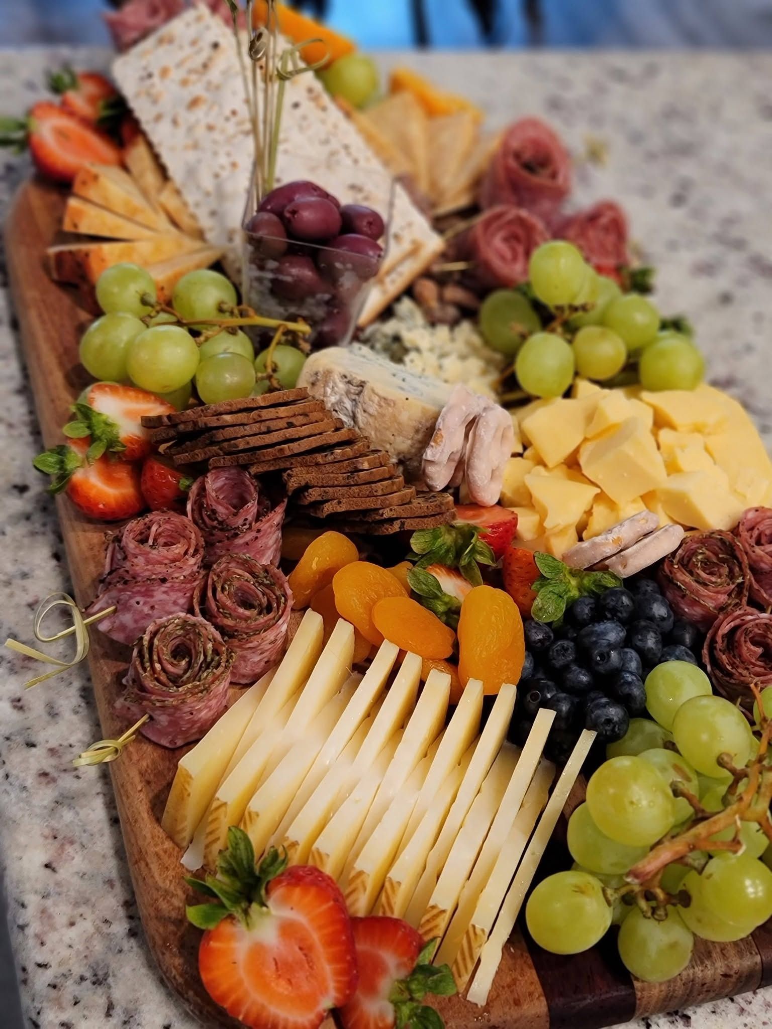 Charcuterie board with cheeses, grapes, strawberries, crackers, dried fruit, and sliced salami
