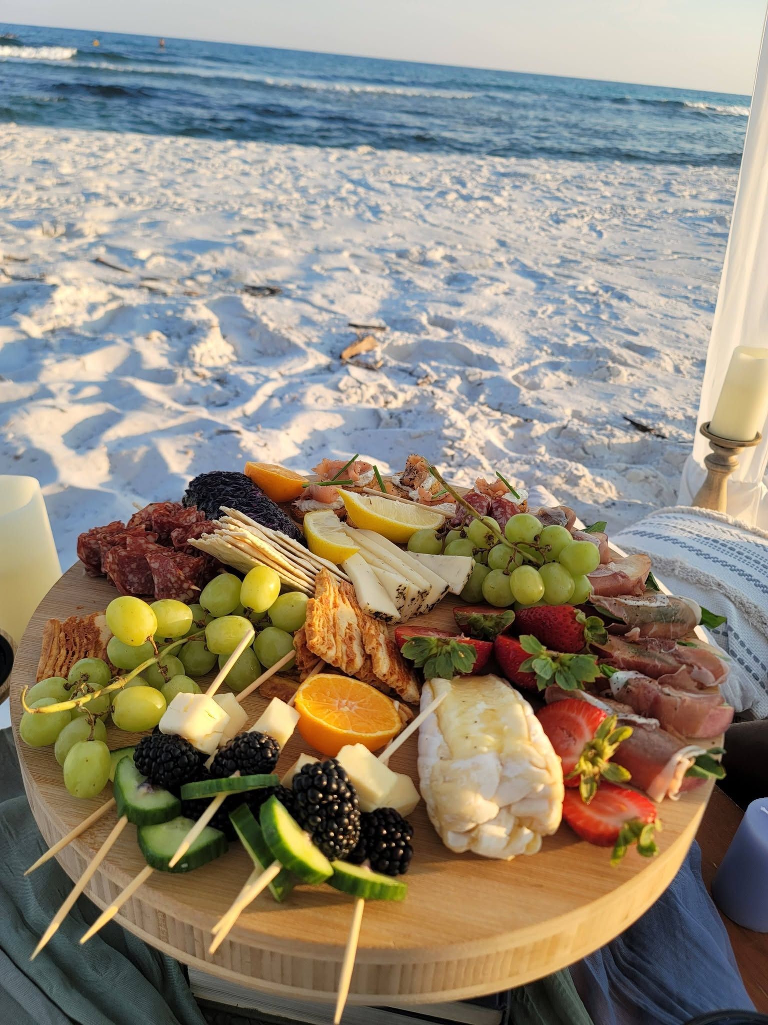 Seafood and fruit platter on a table overlooking a sandy beach and ocean at sunset