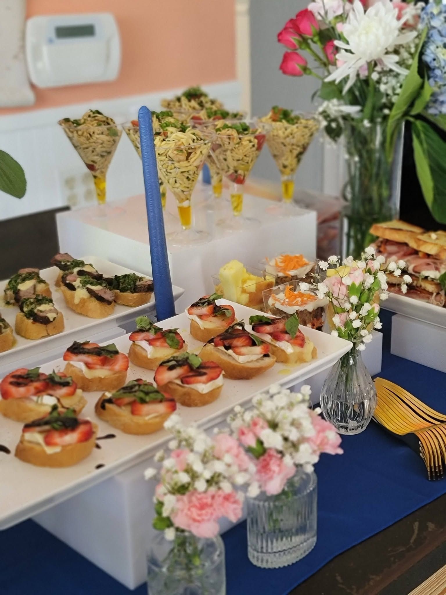 Appetizer buffet with mini tartlets and pastries on white tiered stands, decorated with flowers and blue accents