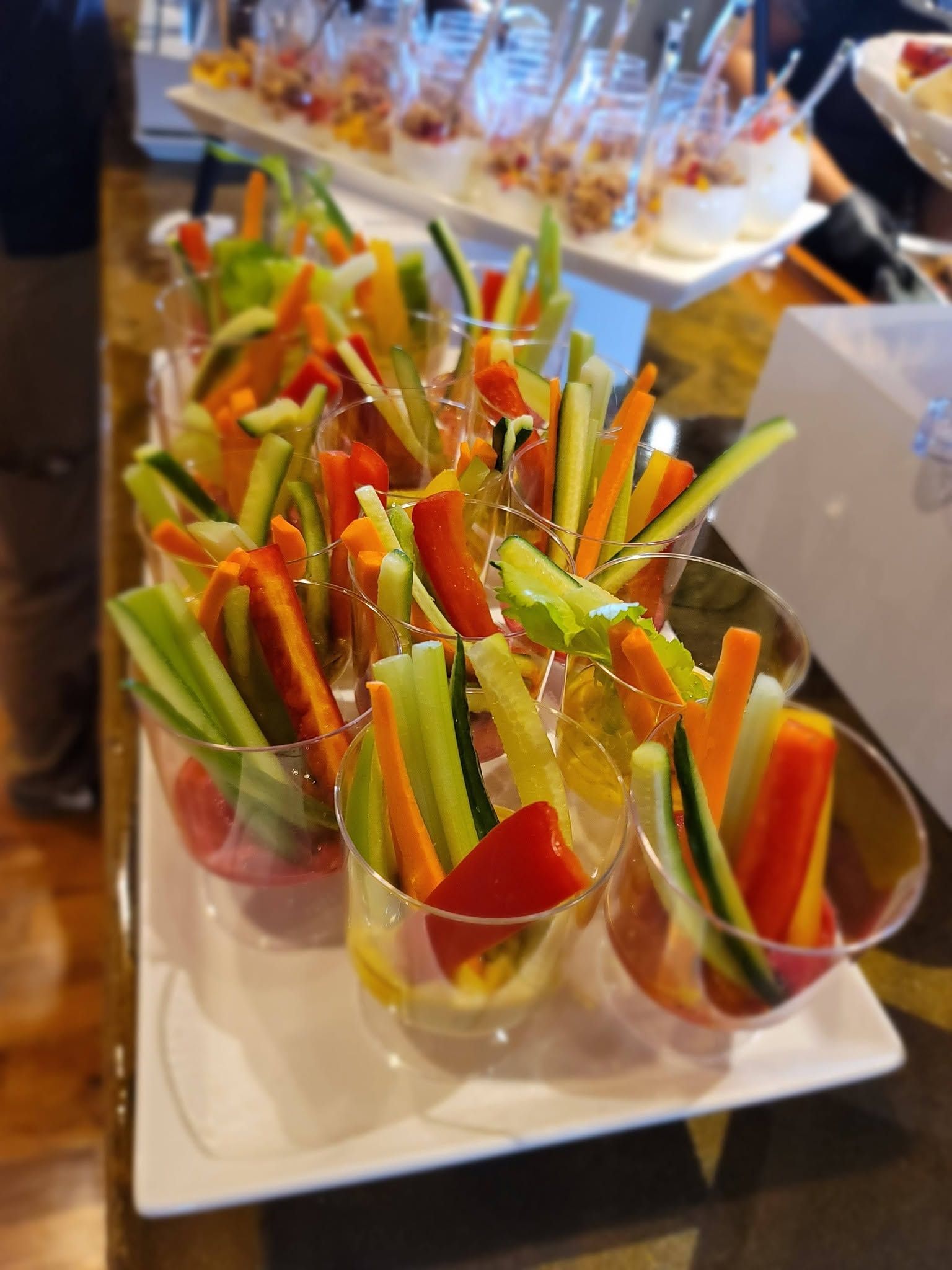 Colorful vegetable crudités in clear cups on a white tray at a buffet