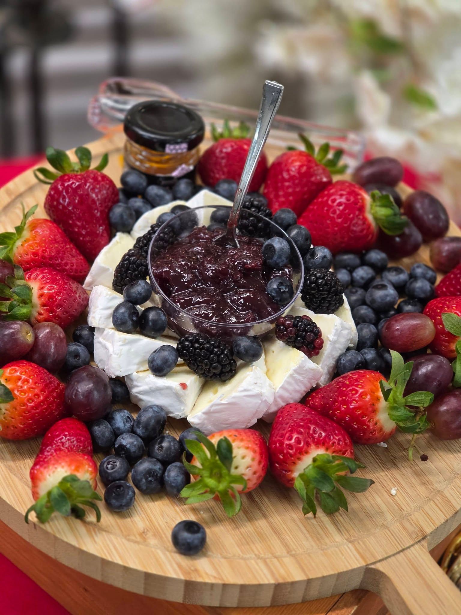 Berry-topped dessert on a wooden board, with whipped cream and assorted fresh berries all around