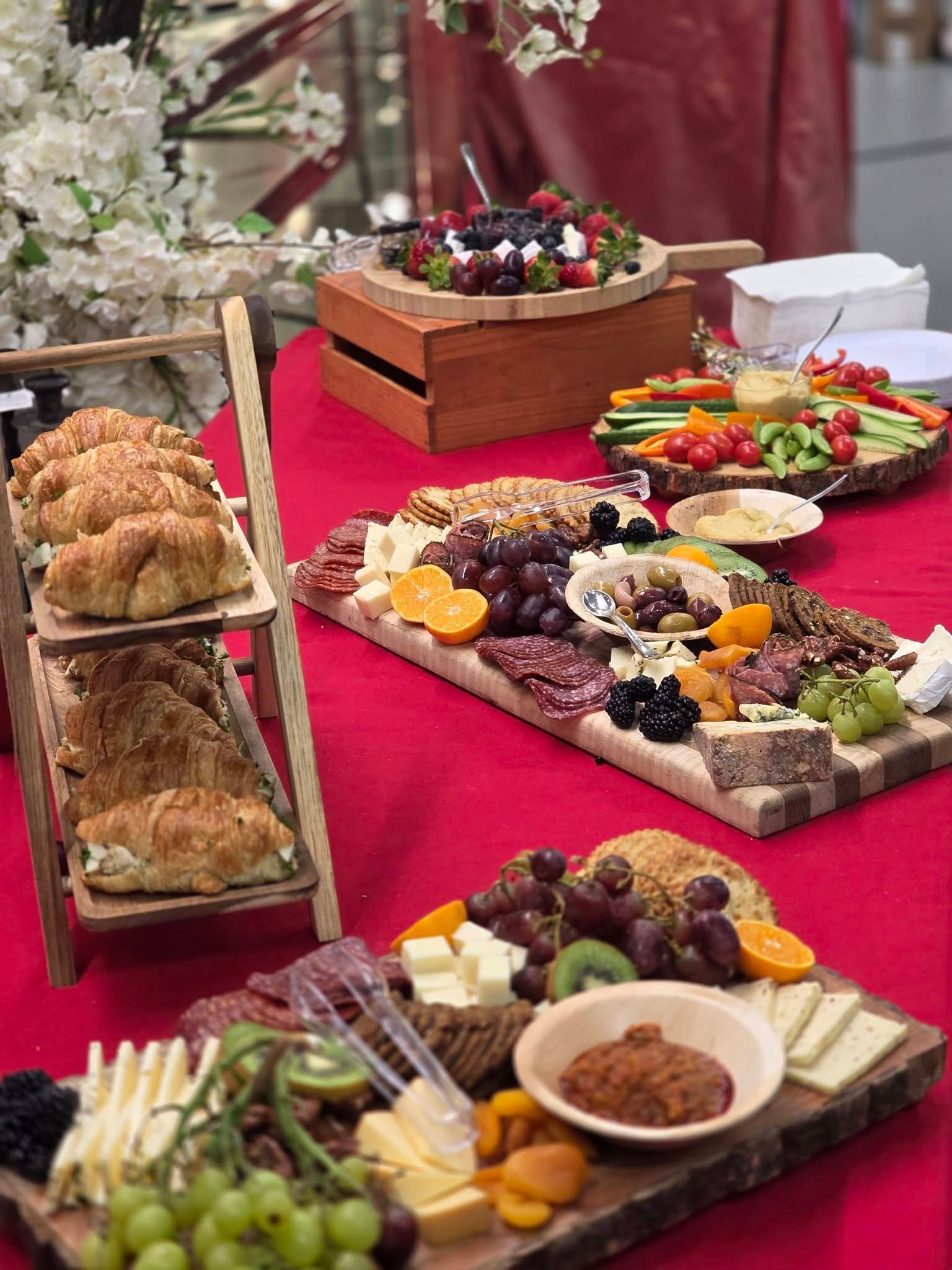 Buffet table with assorted appetizers, cheeses, pastries, and fruit on red tablecloth