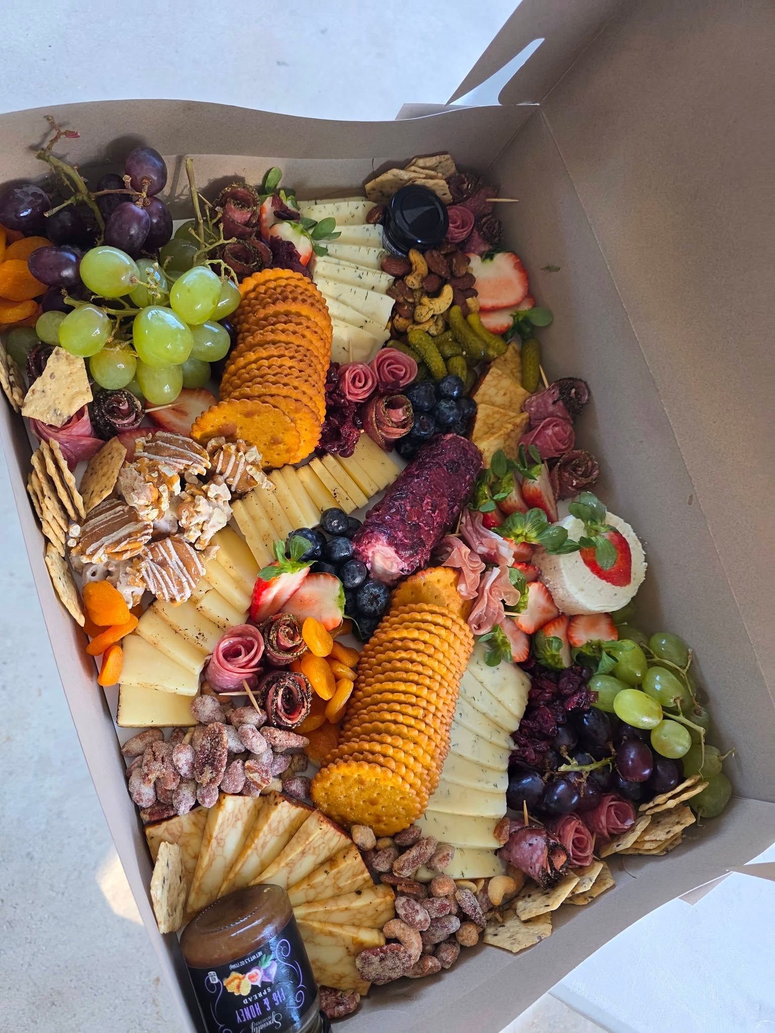 Assorted cheese, grapes, crackers, fruit, and nuts arranged in a gift box.