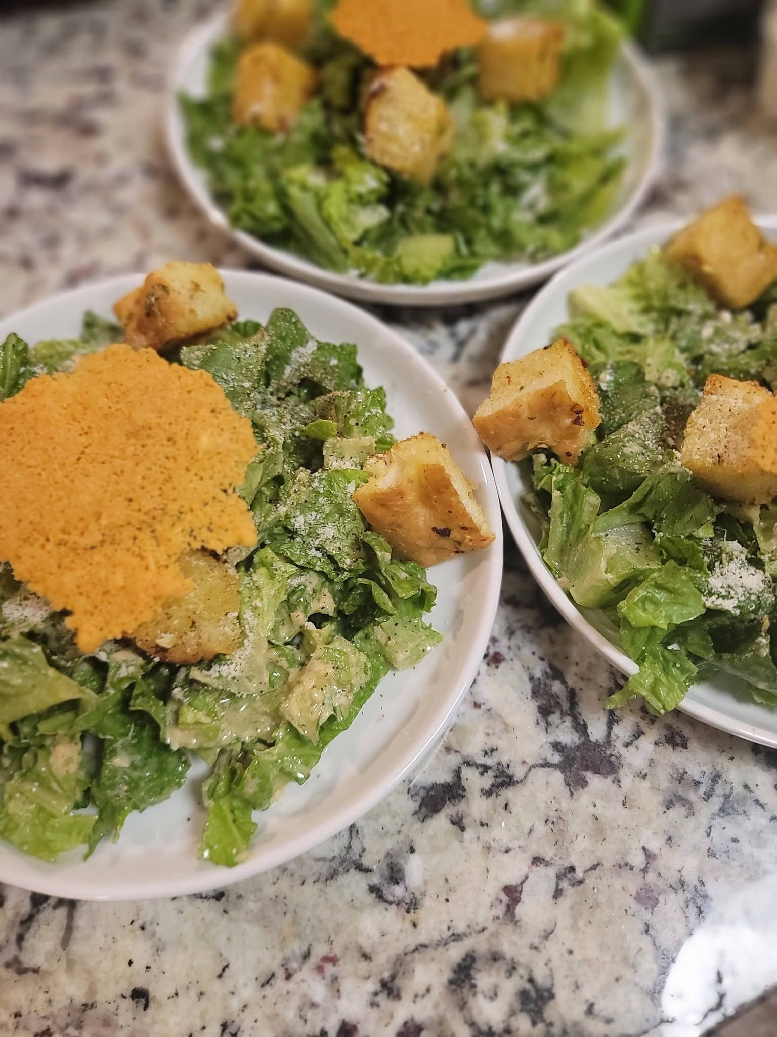 Three bowls of Caesar salad with croutons on a granite countertop