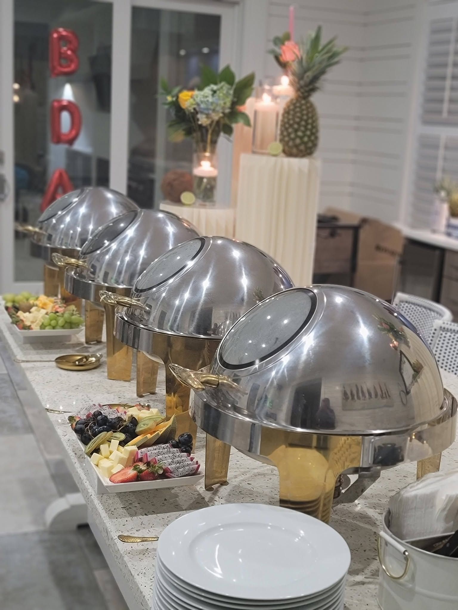 Buffet table with silver chafing dishes, salad toppings, and white plates in a bright dining room