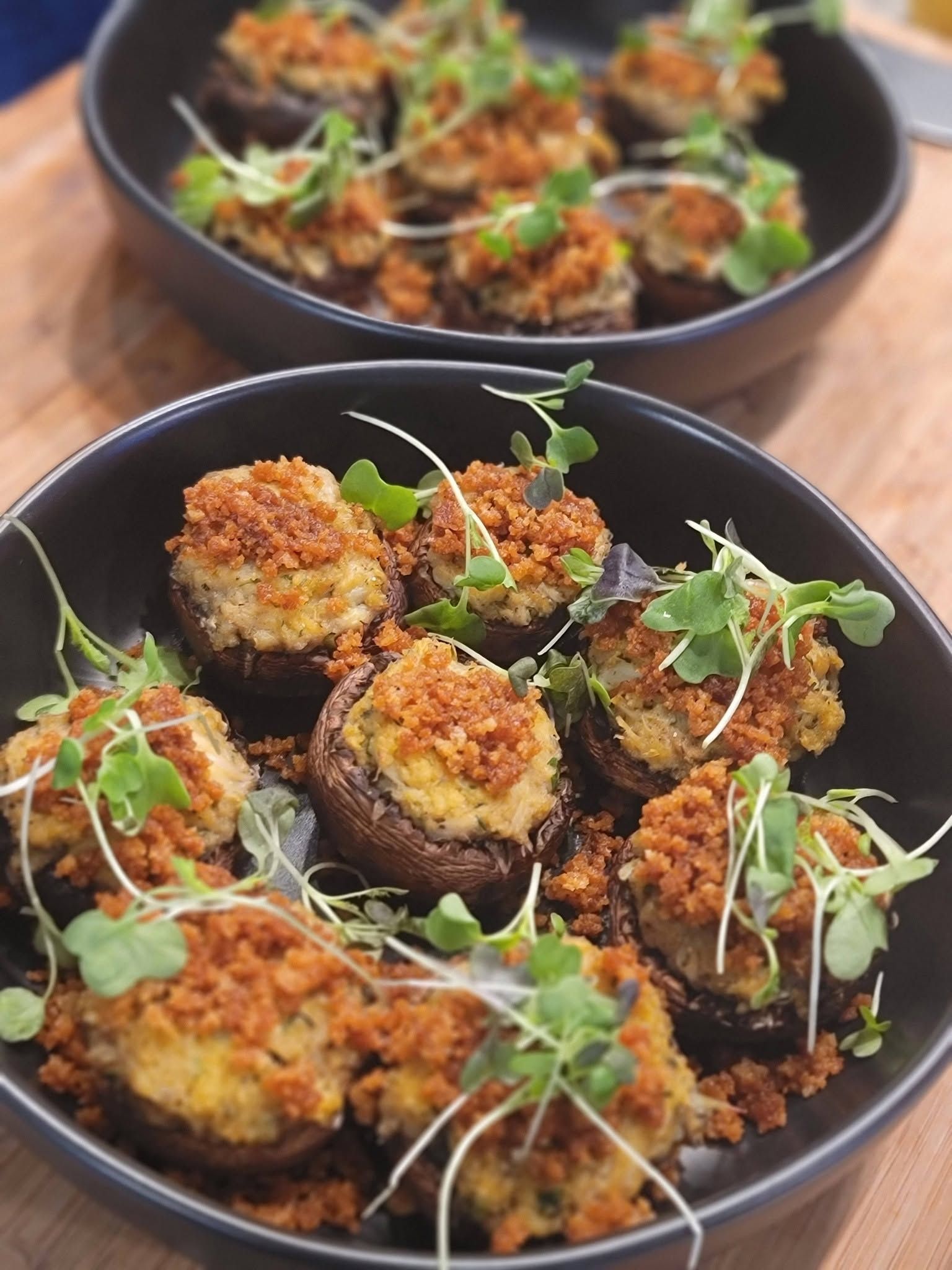 Two bowls of crispy baked eggplant bites topped with herbs and microgreens on a wooden table