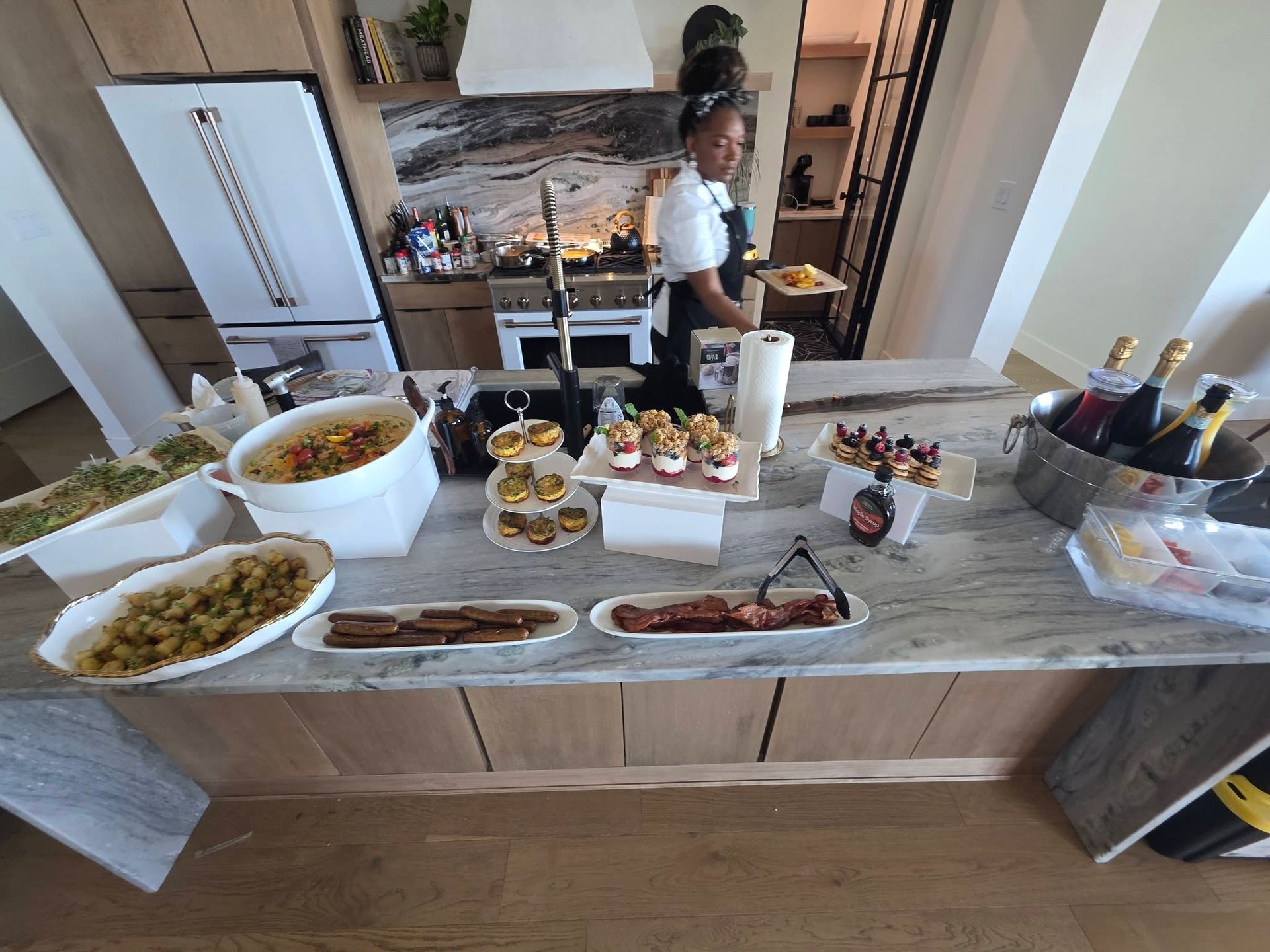 Buffet table with assorted dishes and drinks in a home kitchen, with a person standing in the background