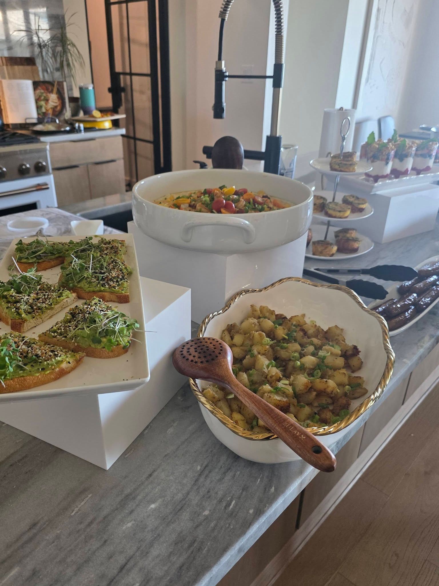 Buffet table with bowls of salad, bread with green spread, and a serving spoon in a kitchen.