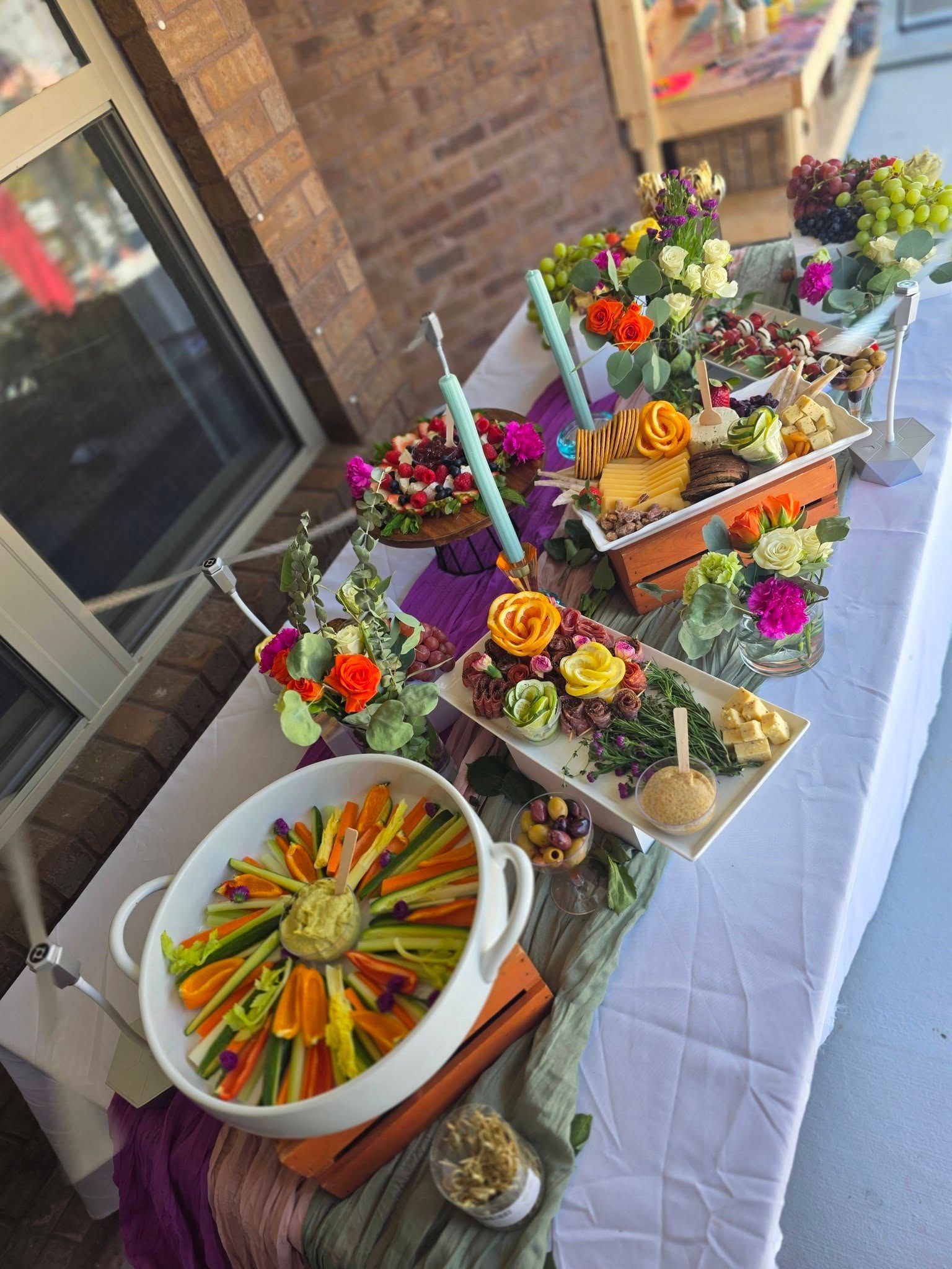 Outdoor buffet table with colorful floral centerpieces and platters of sliced fruit and vegetables