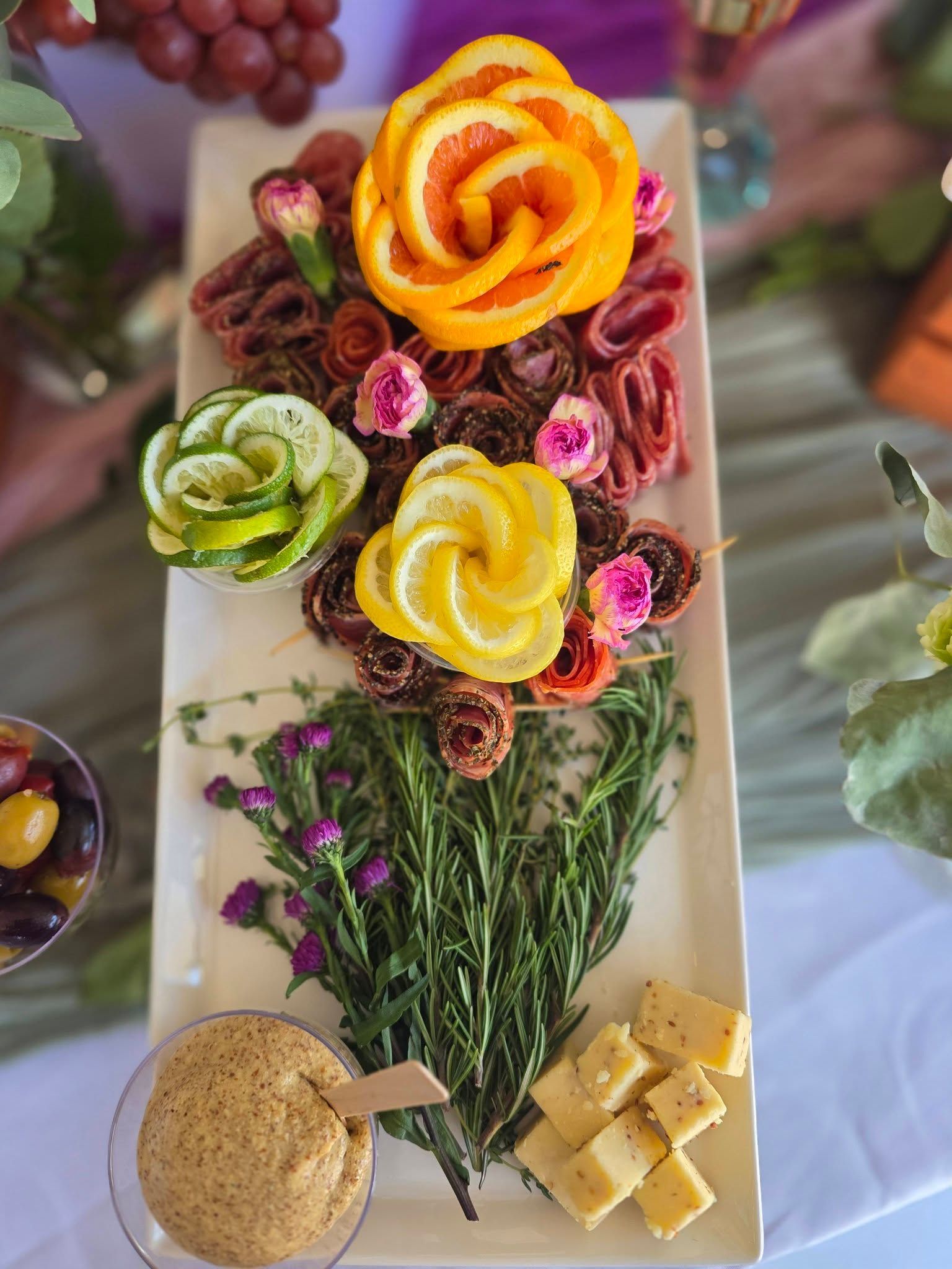 Colorful flower-shaped vegetable platter with herbs, crackers, dip, and cheese on a white tray