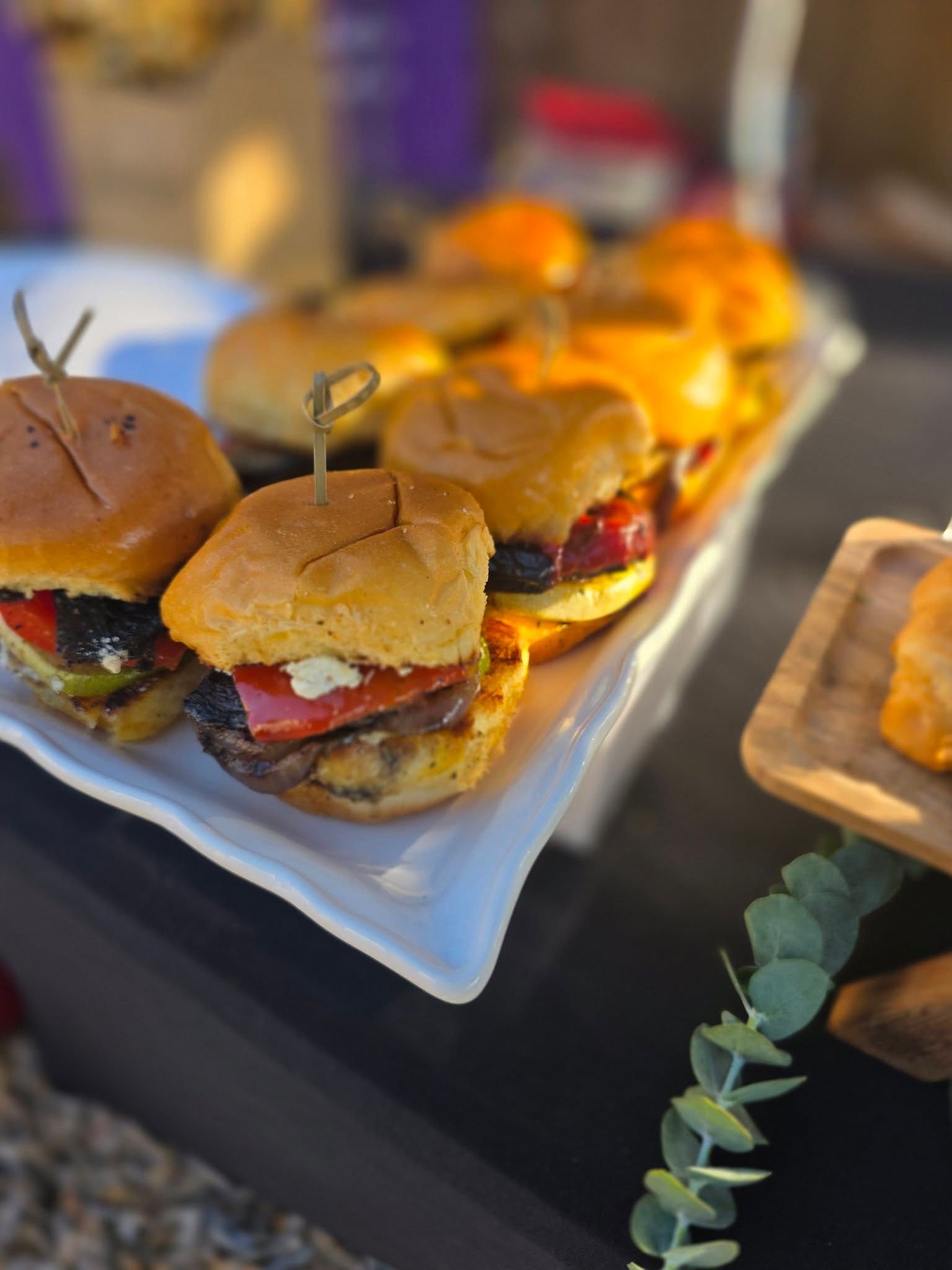 Tray of mini burgers with toothpicks on a white platter at a party table