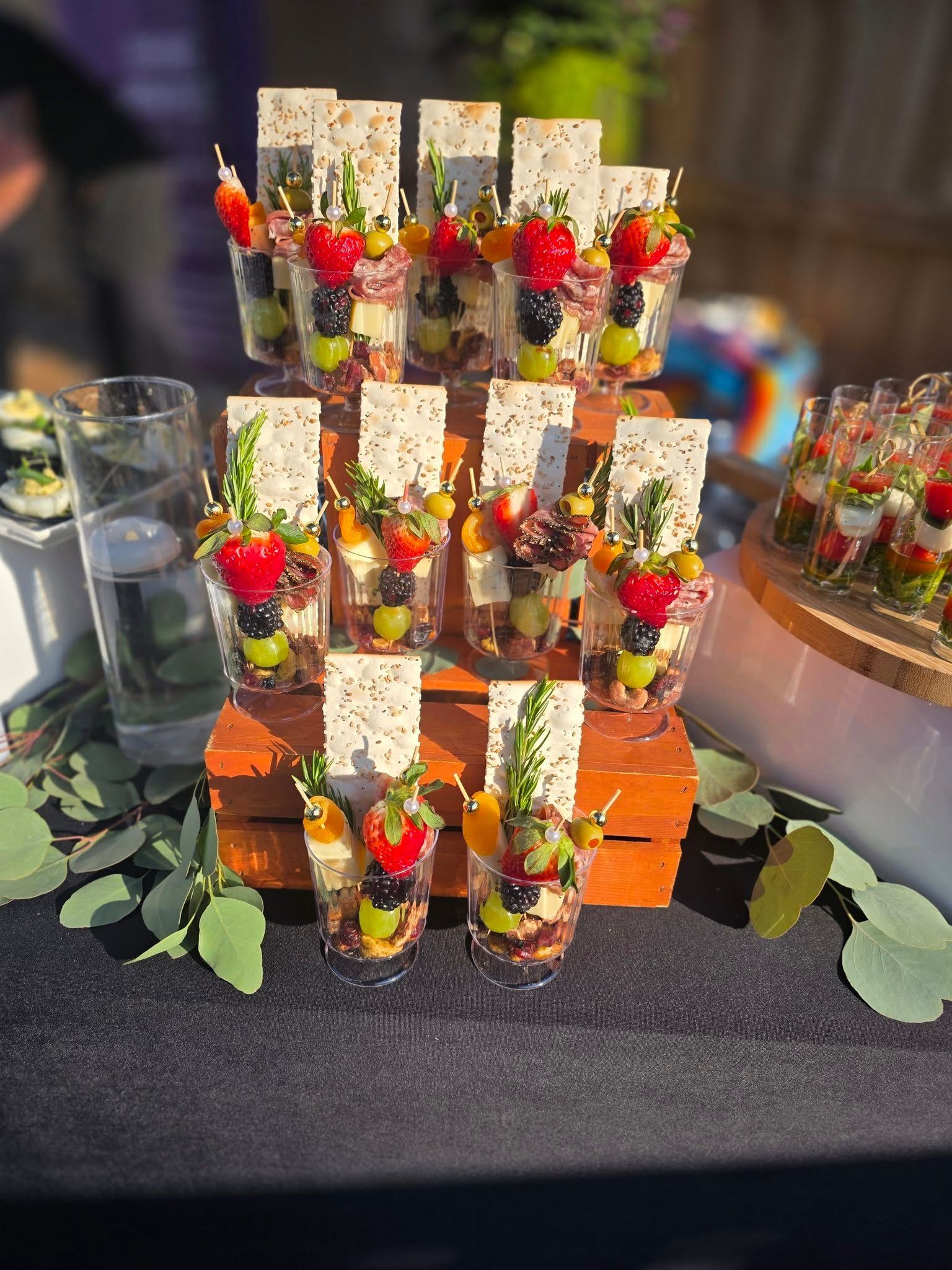 Mini dessert cups topped with berries and white chocolate on a tiered display at an event table