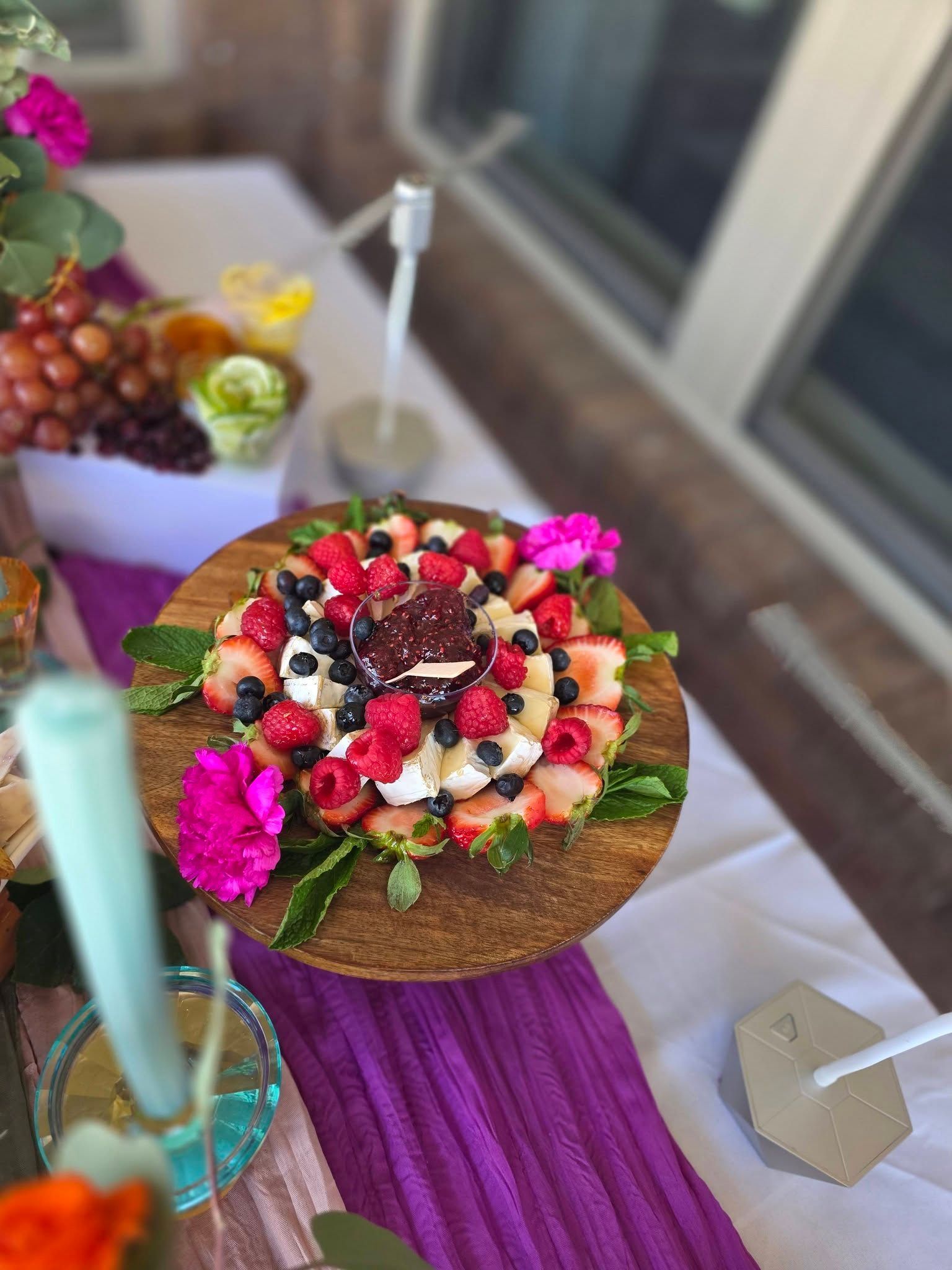Decorated fruit tart with berries and flowers on a purple tablecloth at a party table