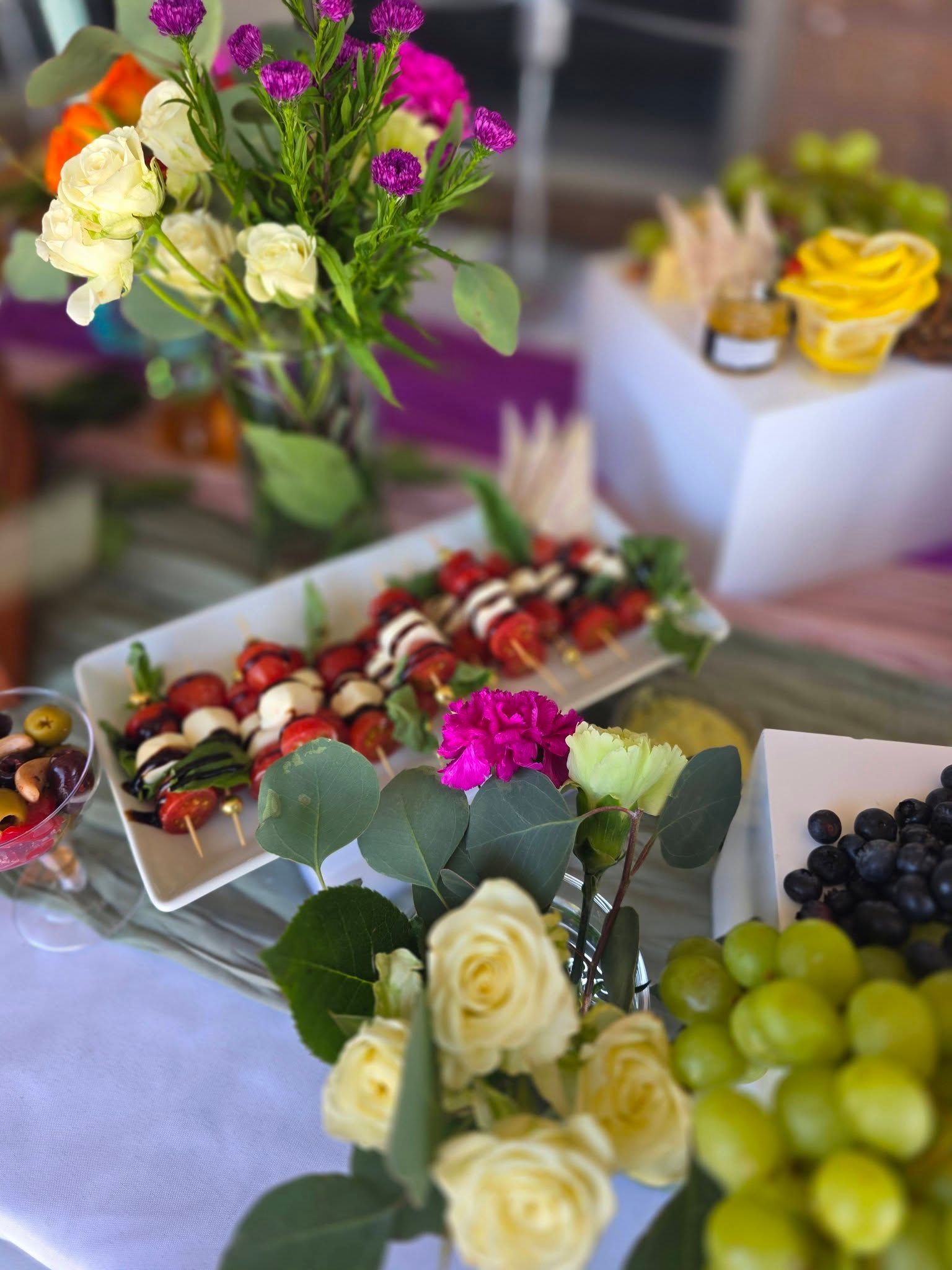 Flower arrangements and fruit platters on a buffet table with white roses and grapes