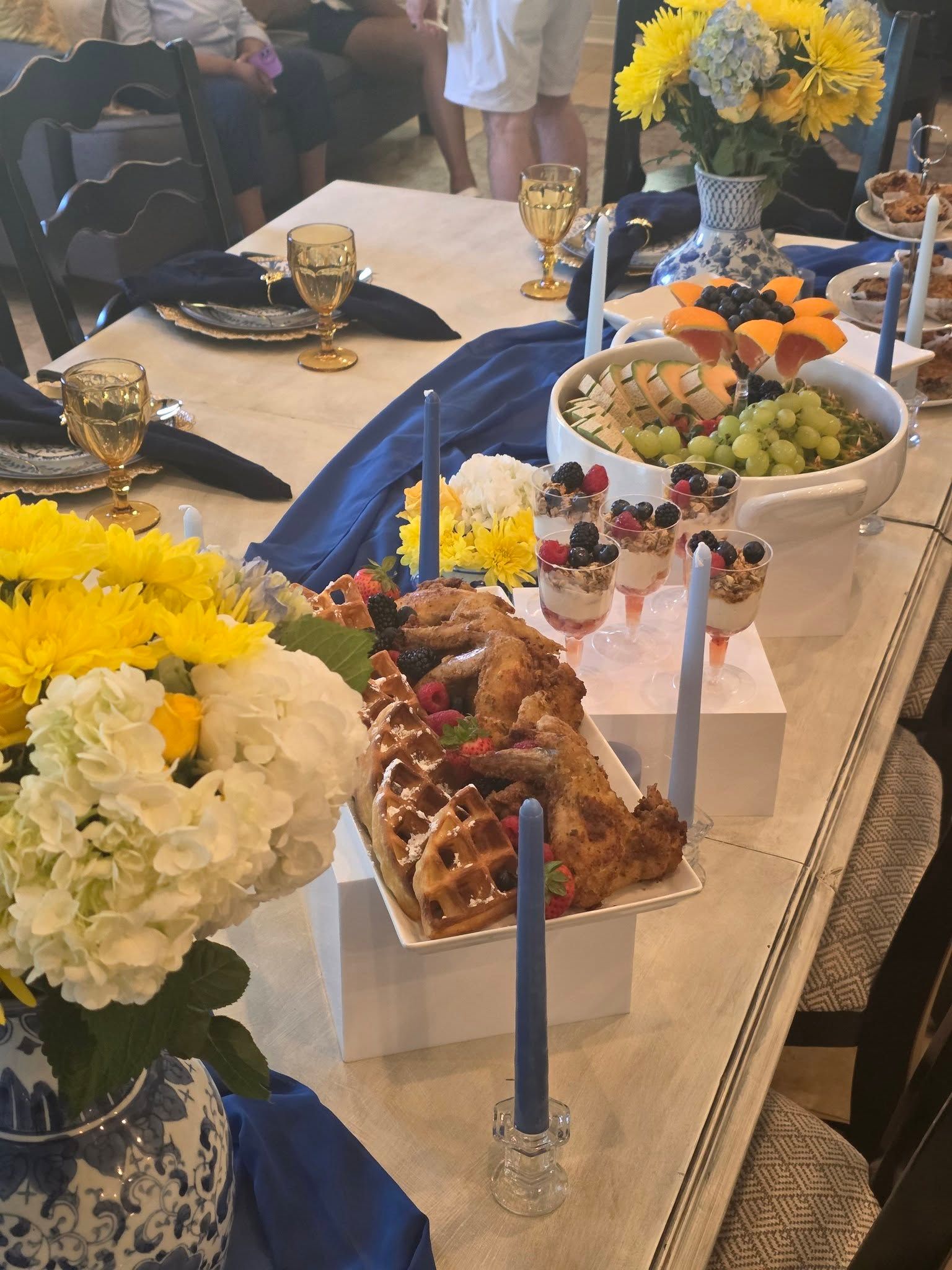 Banquet table with yellow and white floral centerpieces, desserts, fruit, and blue candles at an event