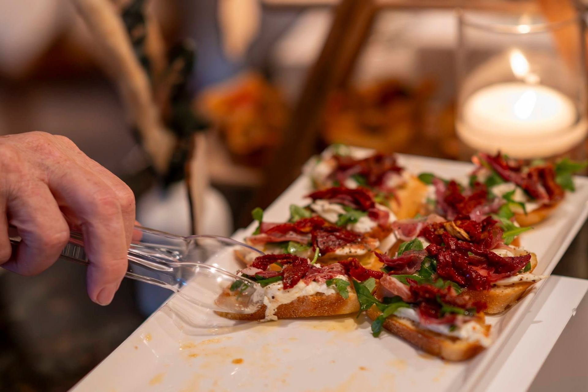 Hand placing a slice of pizza on a white serving tray at a dinner table with candles