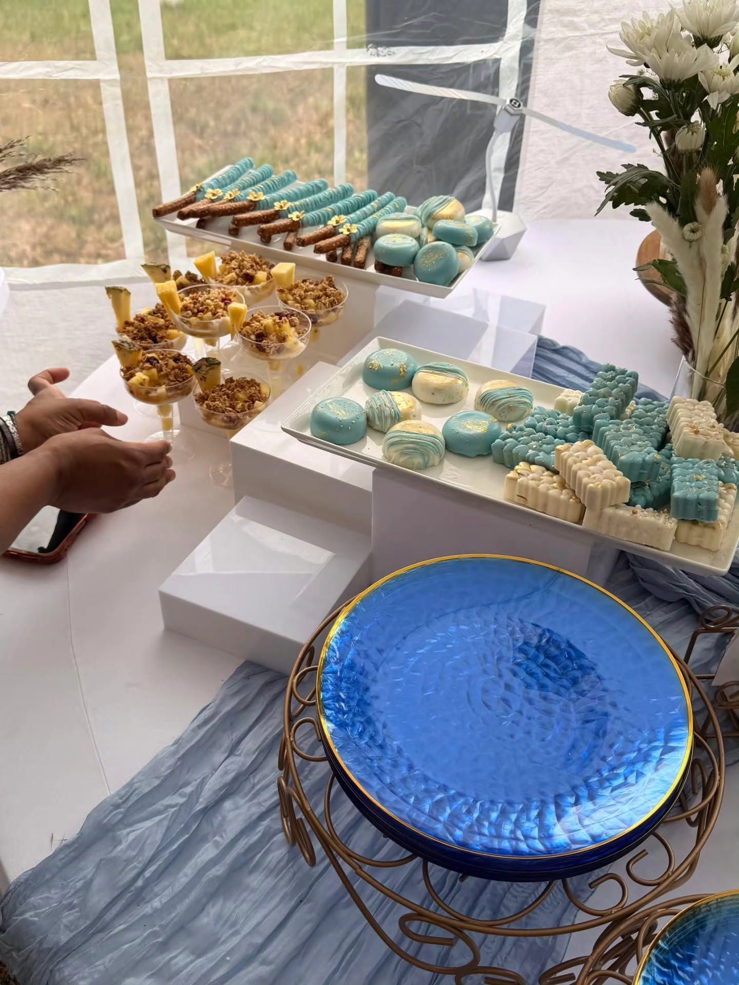 Dessert display with blue, gold, and white pastries on tiered stands beside a blue glass plate