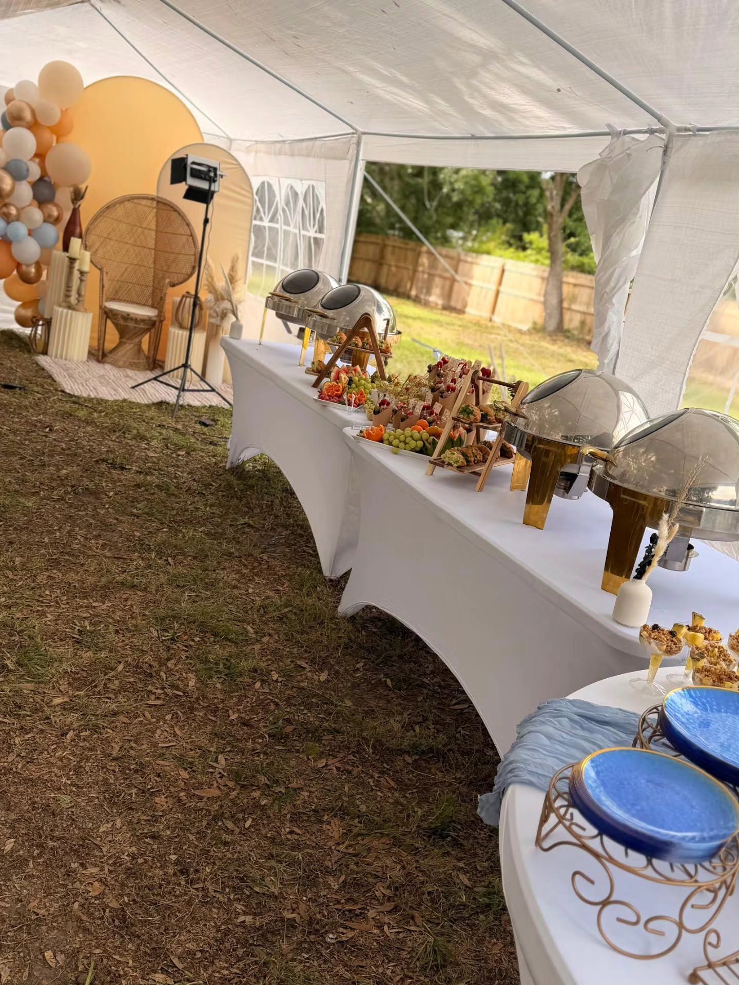 Decorated buffet table under a white tent with gold and white party decor and floral centerpieces