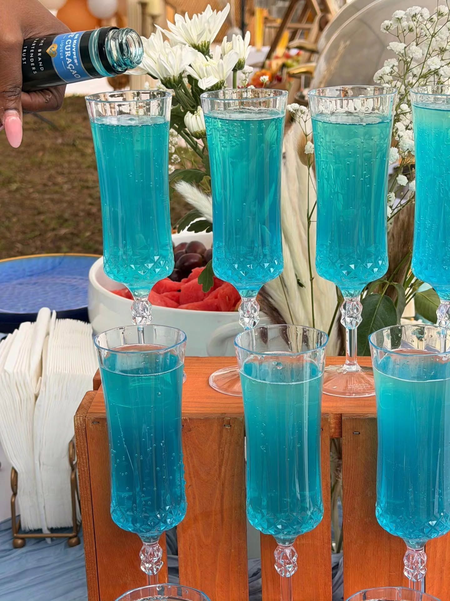 Blue cocktails being poured into champagne flutes on a decorated outdoor table