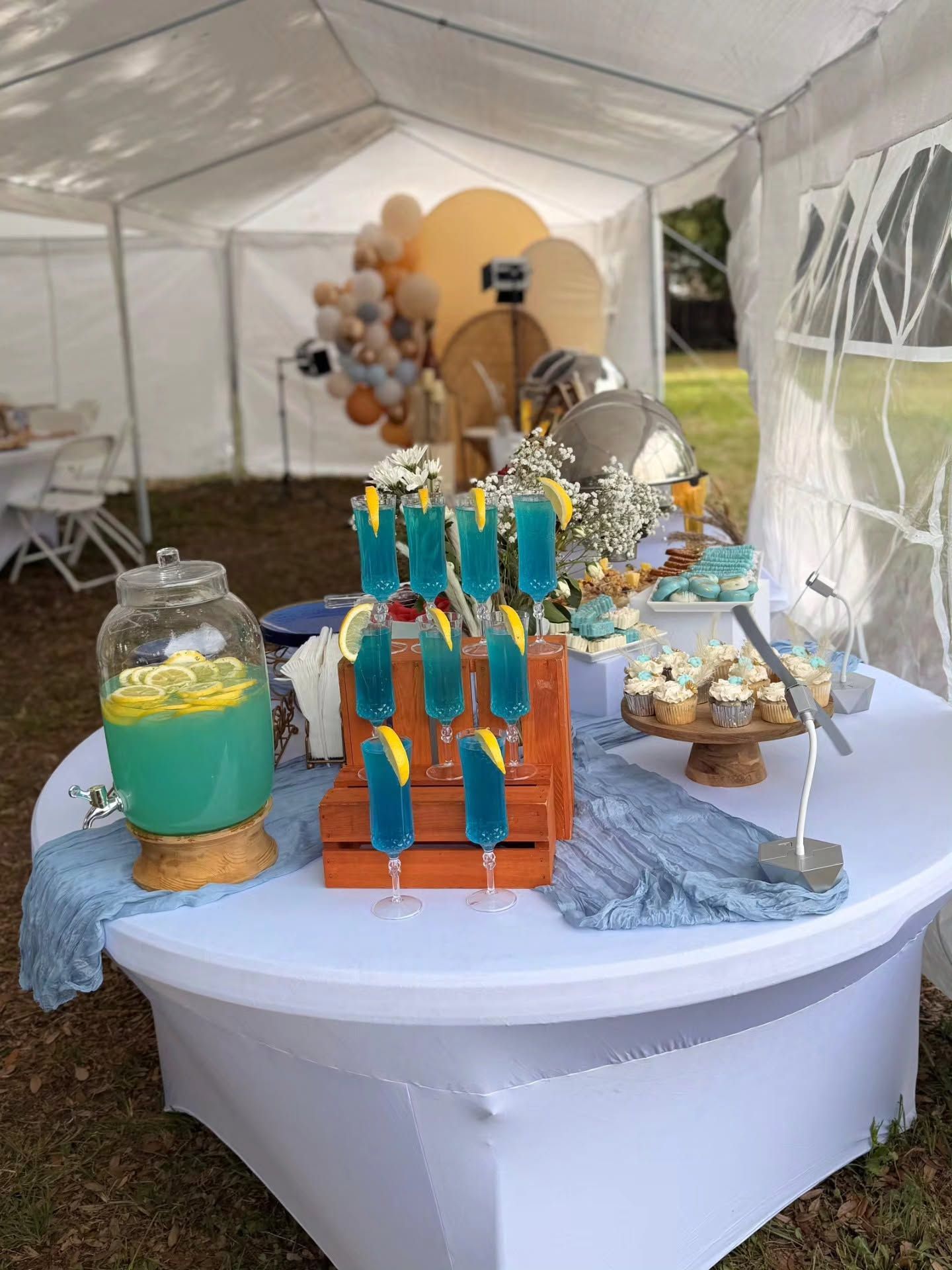Dessert display on a round table under a white tent, with colorful treats, jars, and balloon decorations.