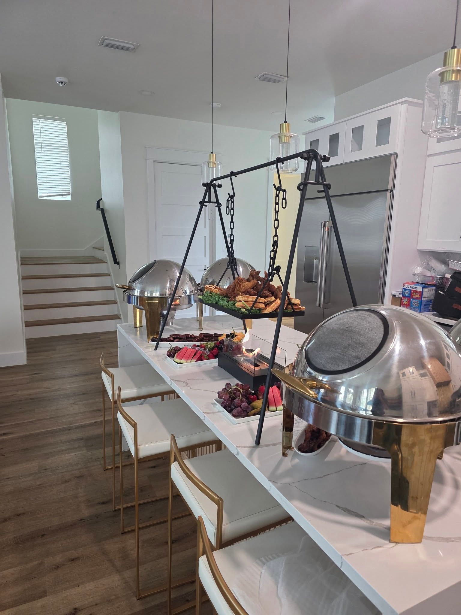 Bright buffet table with covered serving dishes in a modern dining area with wood floors and stairs