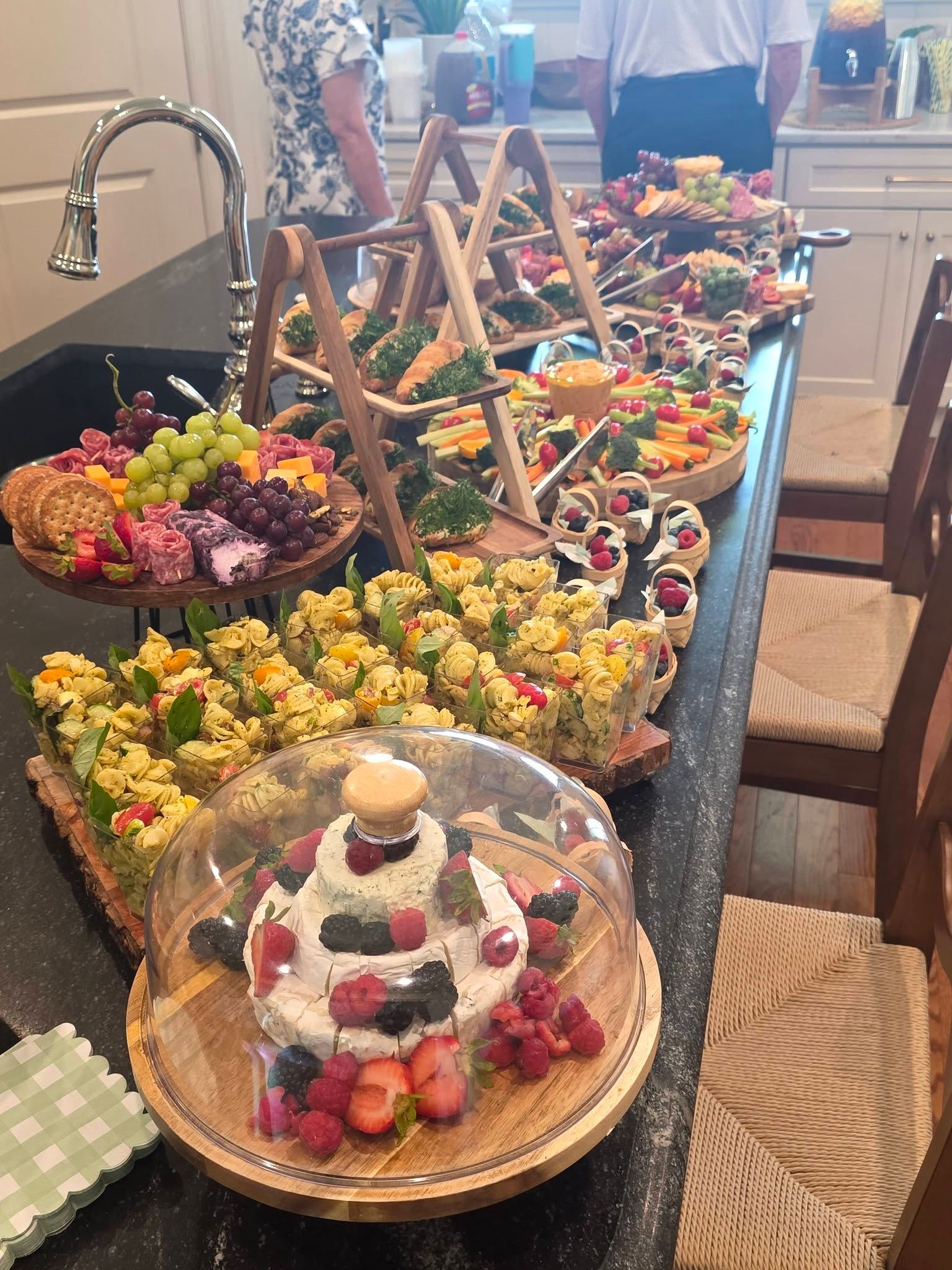 Dessert buffet on a kitchen counter with cakes, fruit tarts, and floral arrangements in woven baskets