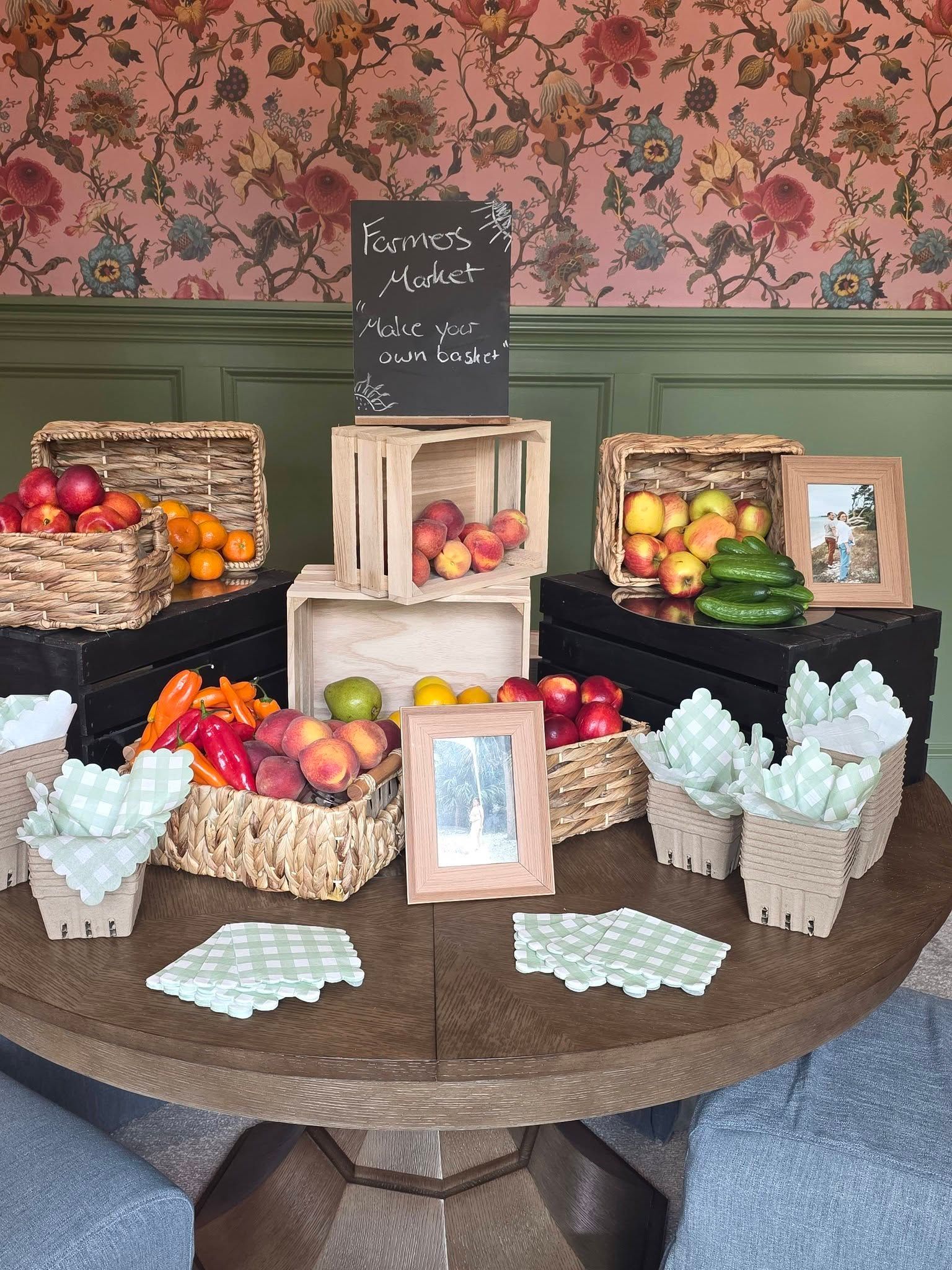 Decorative fruit display on a round table with baskets of apples, oranges, pears, and a chalkboard sign