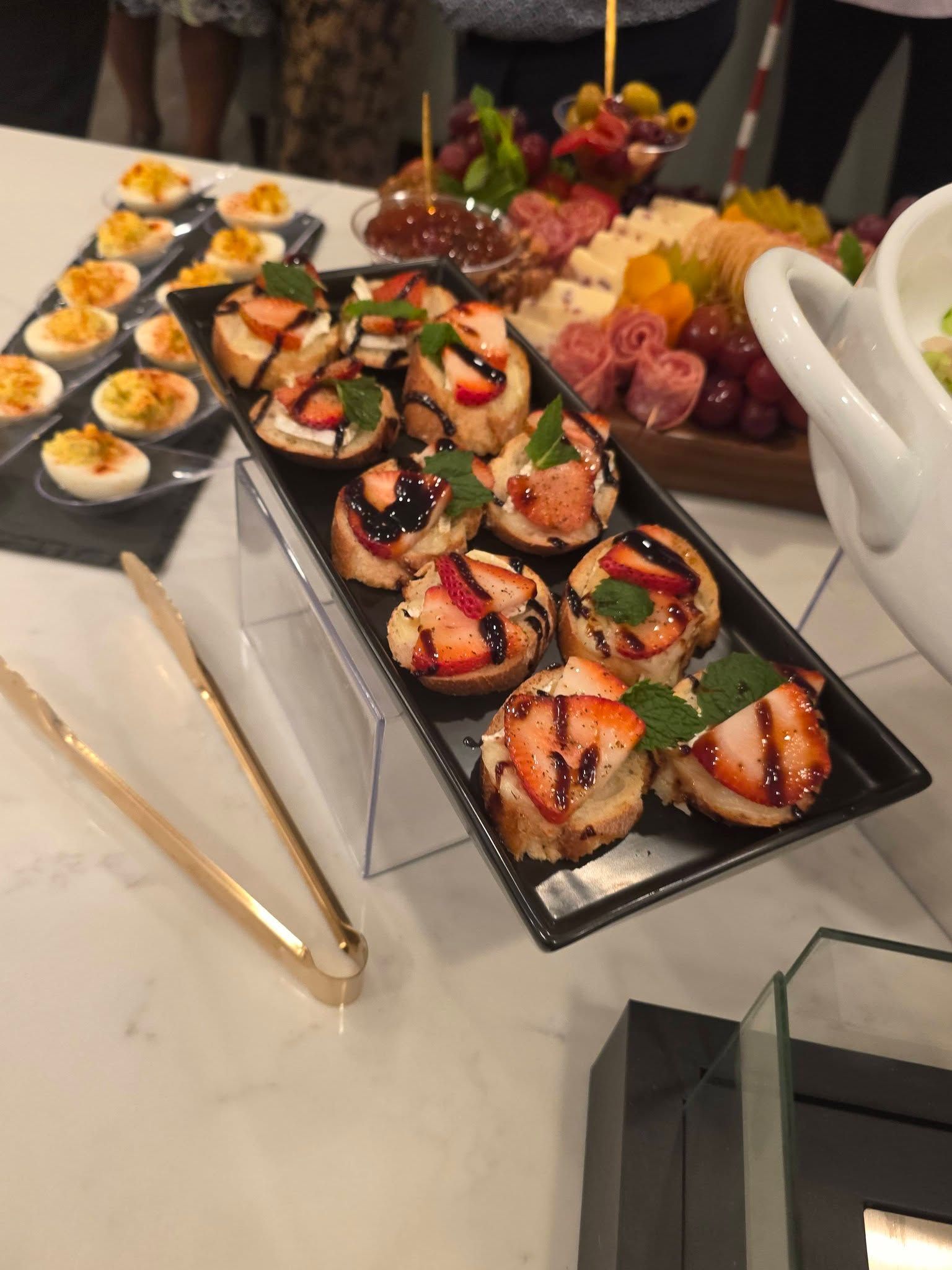 Platter of assorted sushi rolls and sashimi on a buffet table with serving tongs and chopsticks