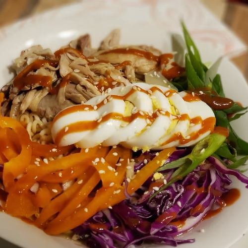 Bowl of rice topped with sliced chicken, orange and purple vegetables, a poached egg, and sesame seeds