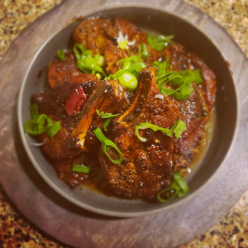 Bowl of dark saucy curry garnished with chopped green onions on a rustic plate