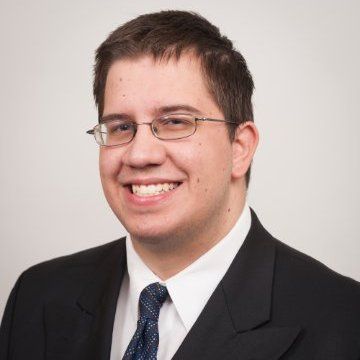Smiling person in glasses and suit, against a light gray background Smiling person in glasses and suit, against a light gray background