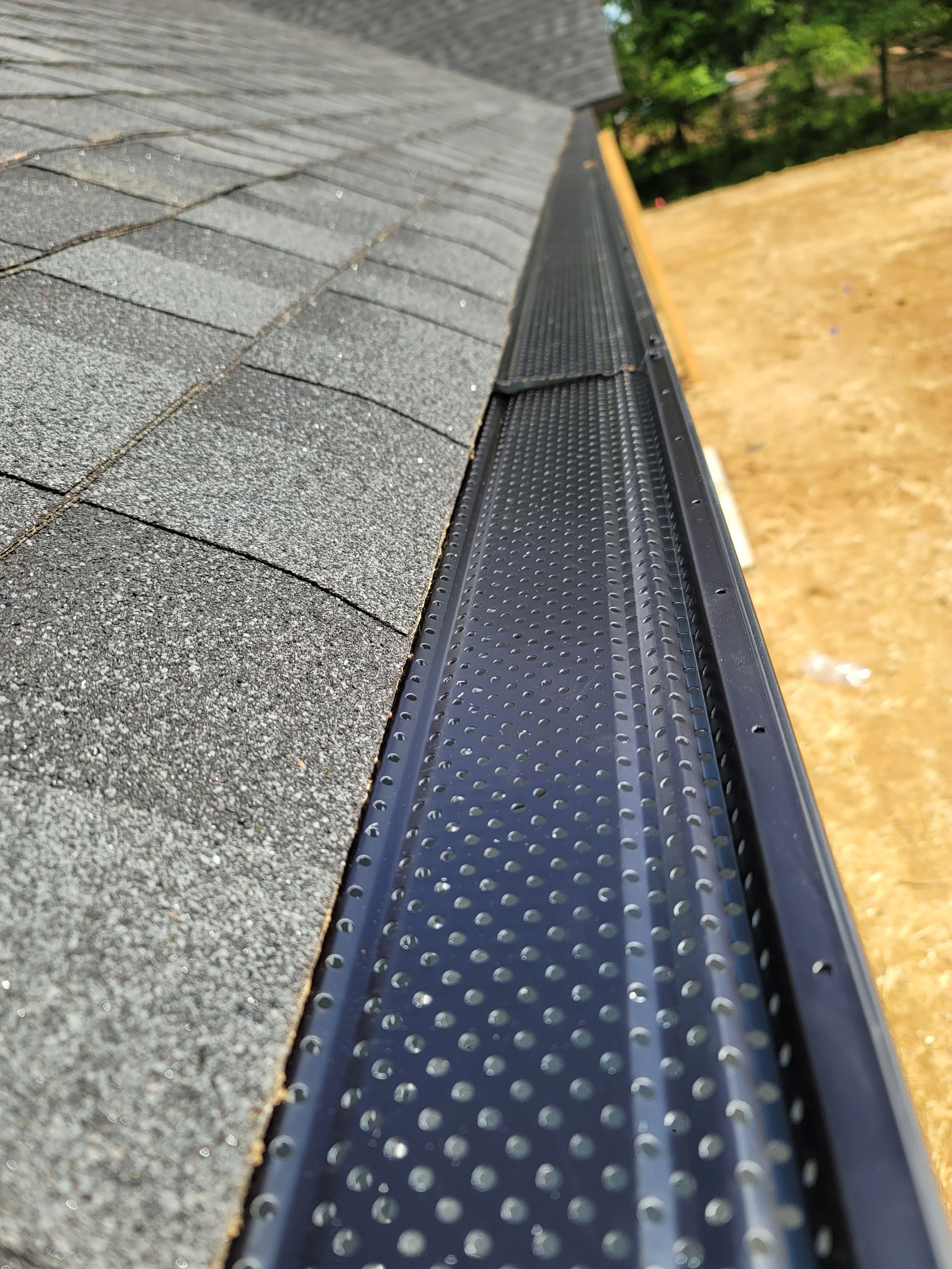 Black gutter guard on a roof with gray shingles, outdoors.