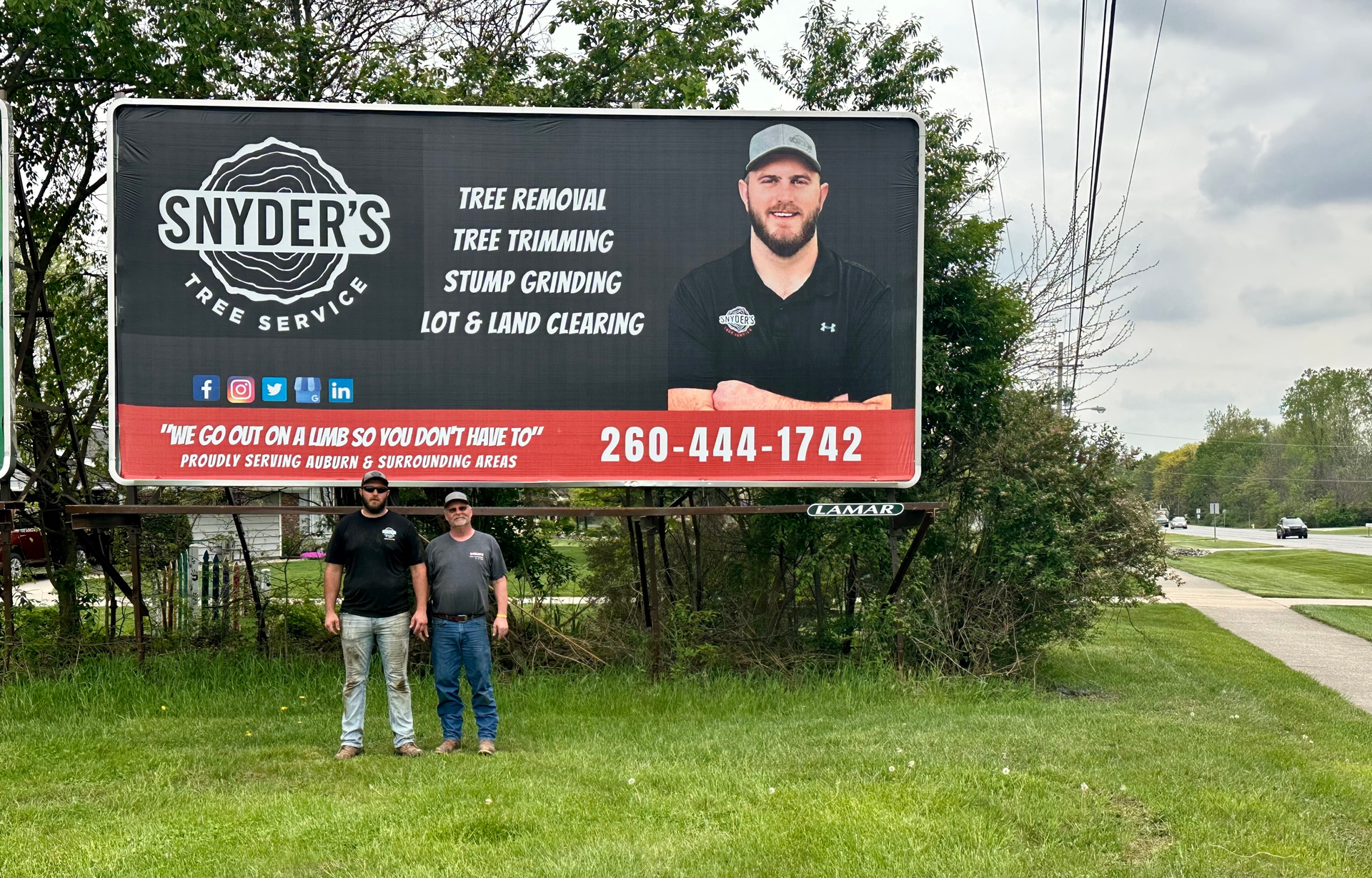Three men standing in front of a billboard advertising Snyder's True Service.